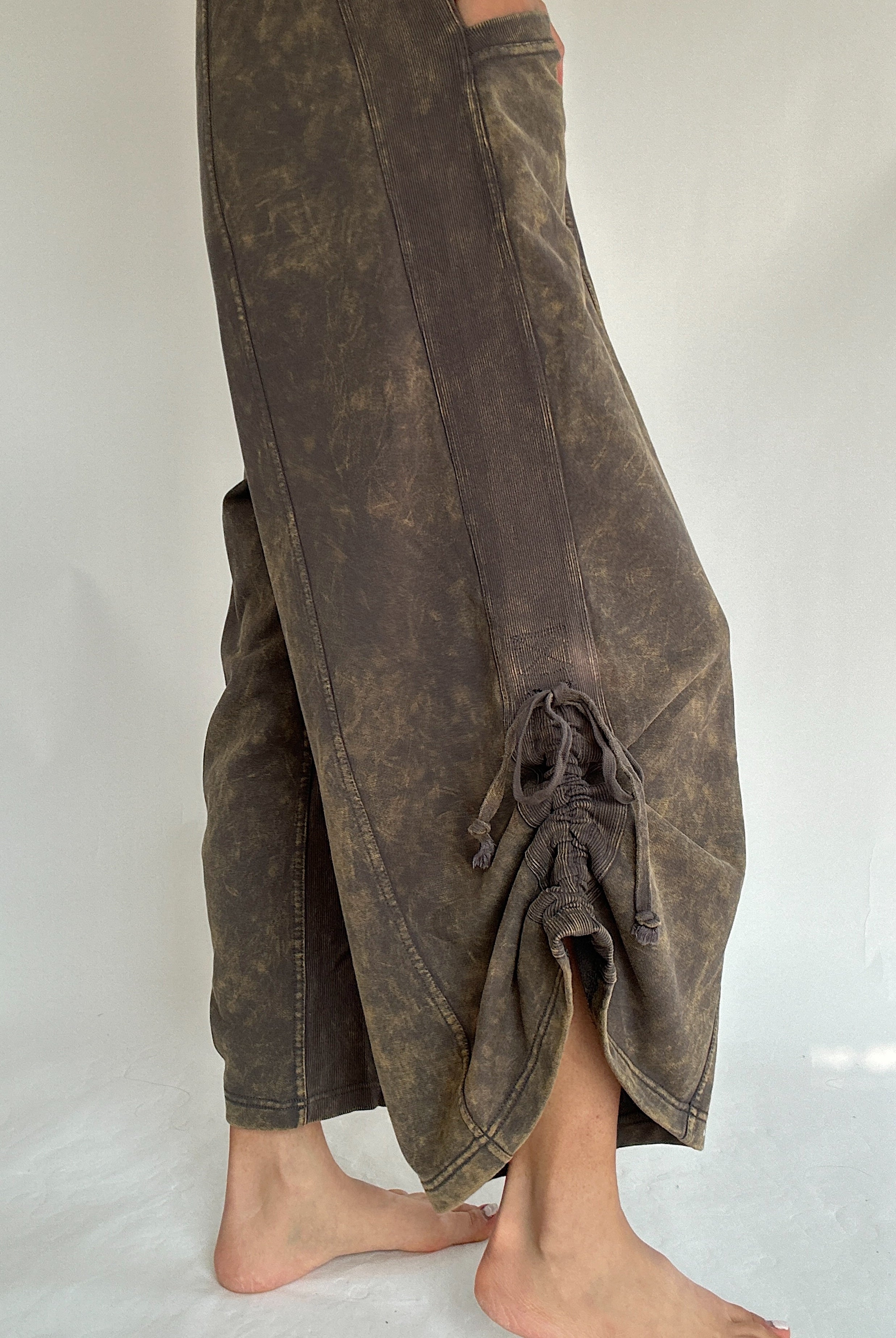 Brown mineral washed jumpsuit on a white background showing the up close detail of the side tie on bottom hem