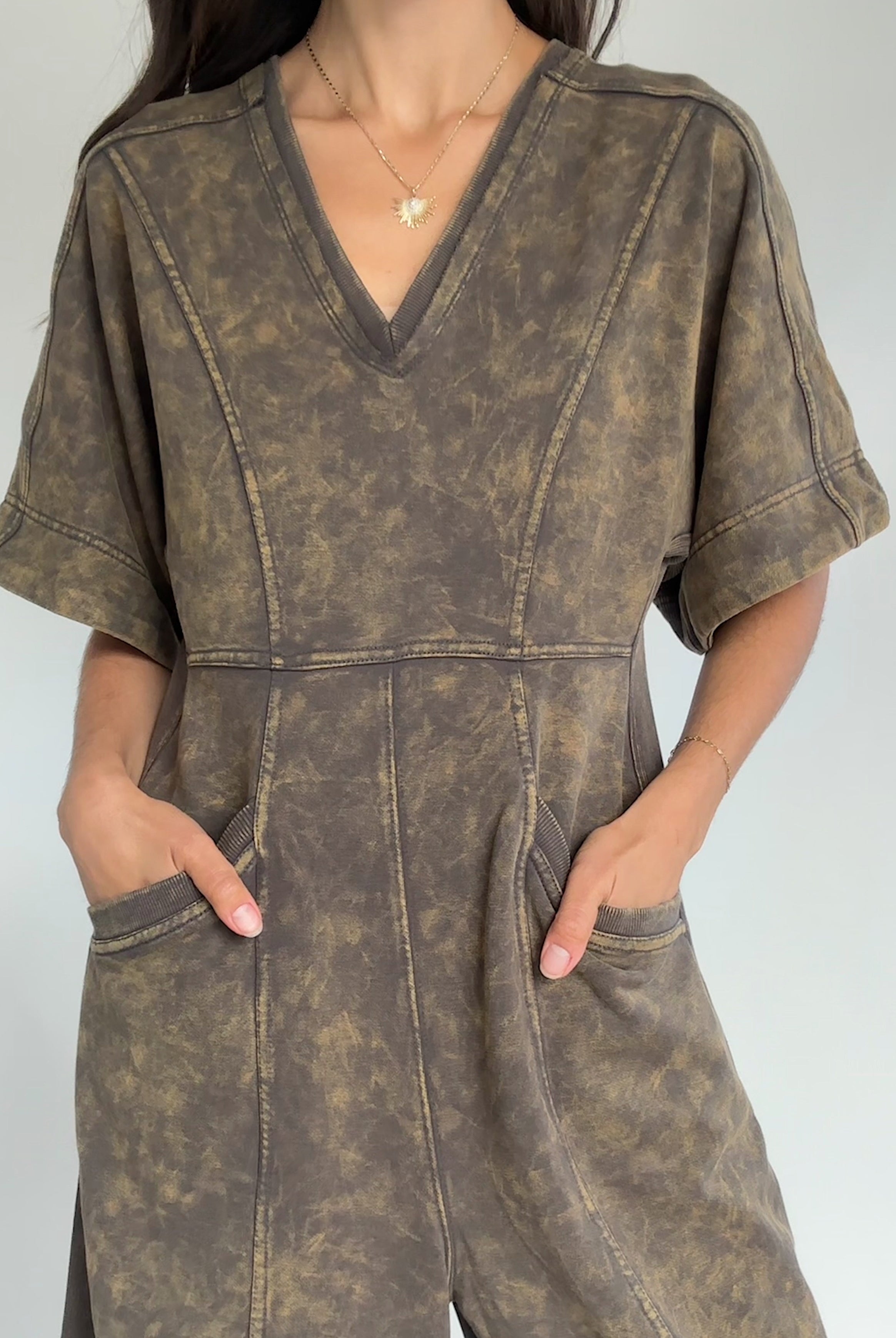 Person wearing a brown mineral-wash jumpsuit against a plain background to show neckline and pockets