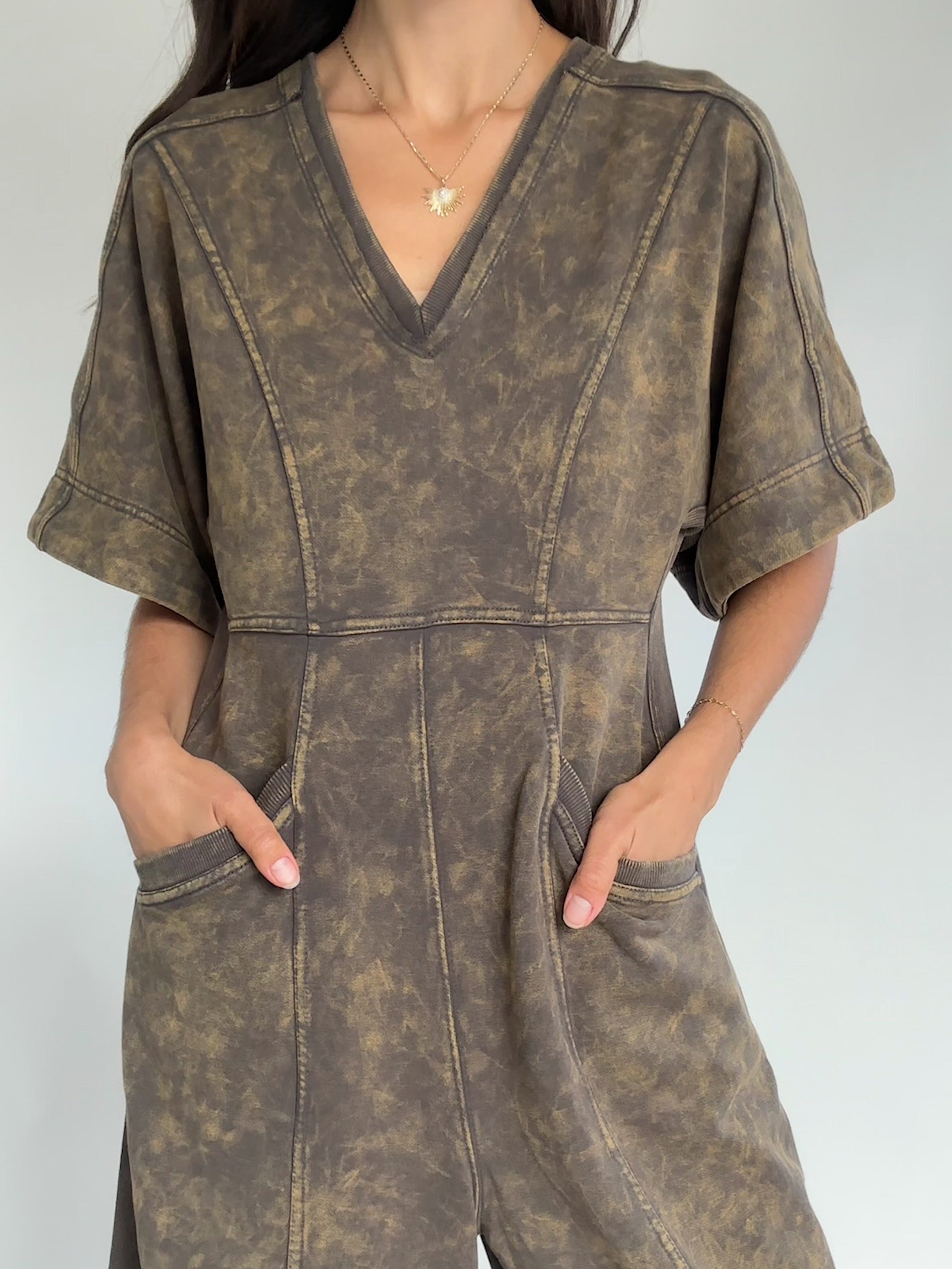 Person wearing a brown mineral-wash jumpsuit against a plain background to show neckline and pockets