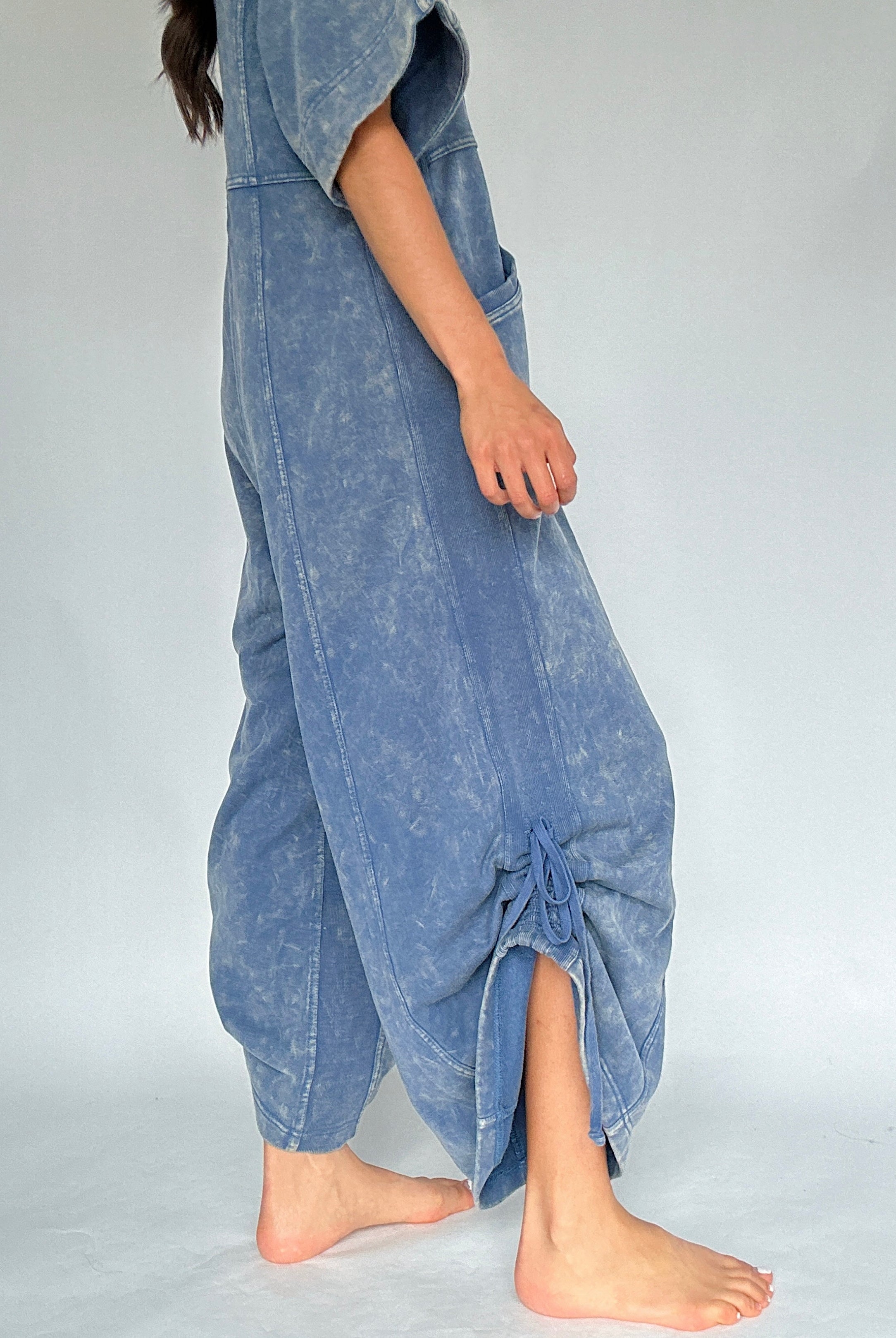 Person wearing a blue jumpsuit with cinched up sides on a plain background