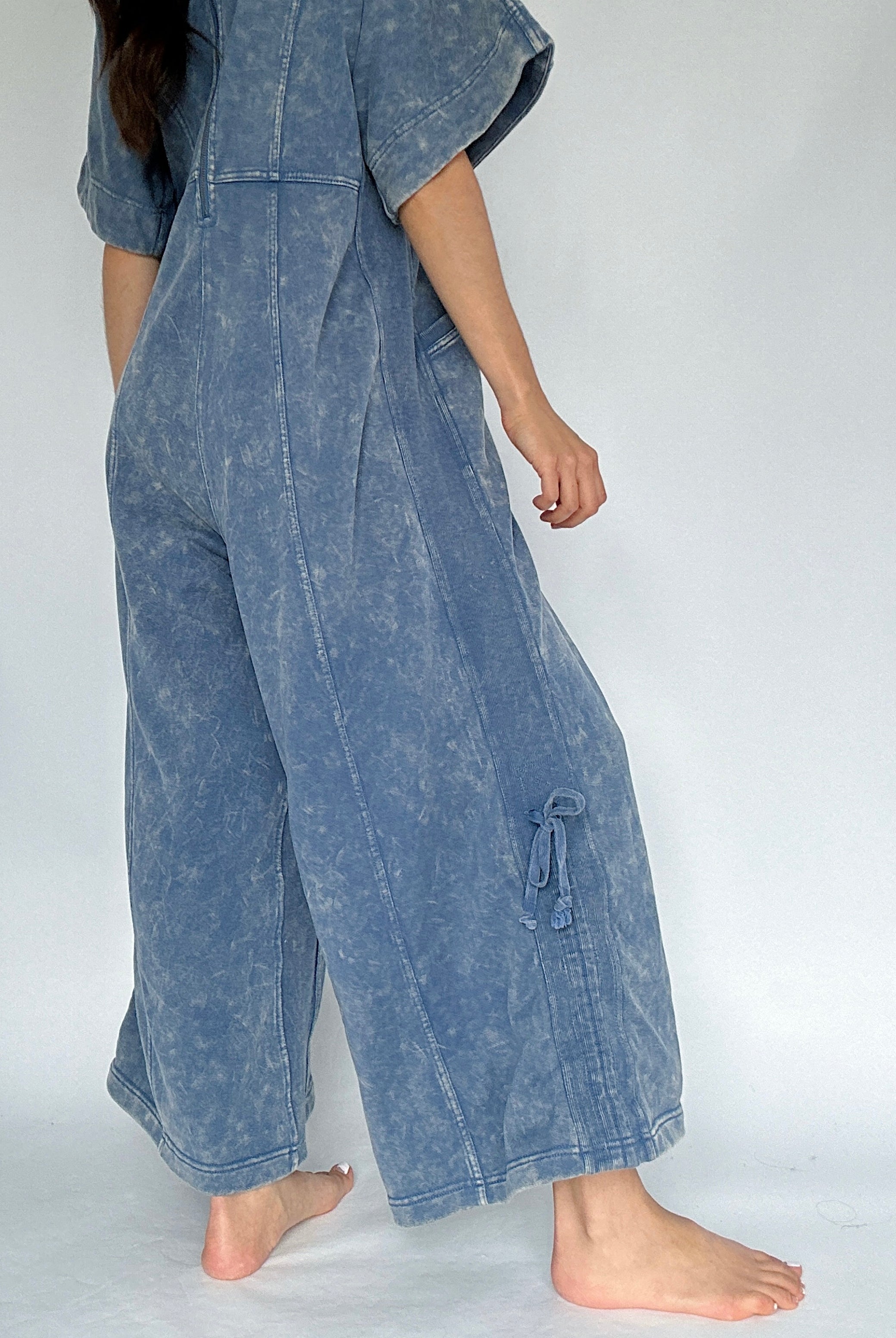 Person wearing a blue acid-wash jumpsuit on a white background to show side tie detail