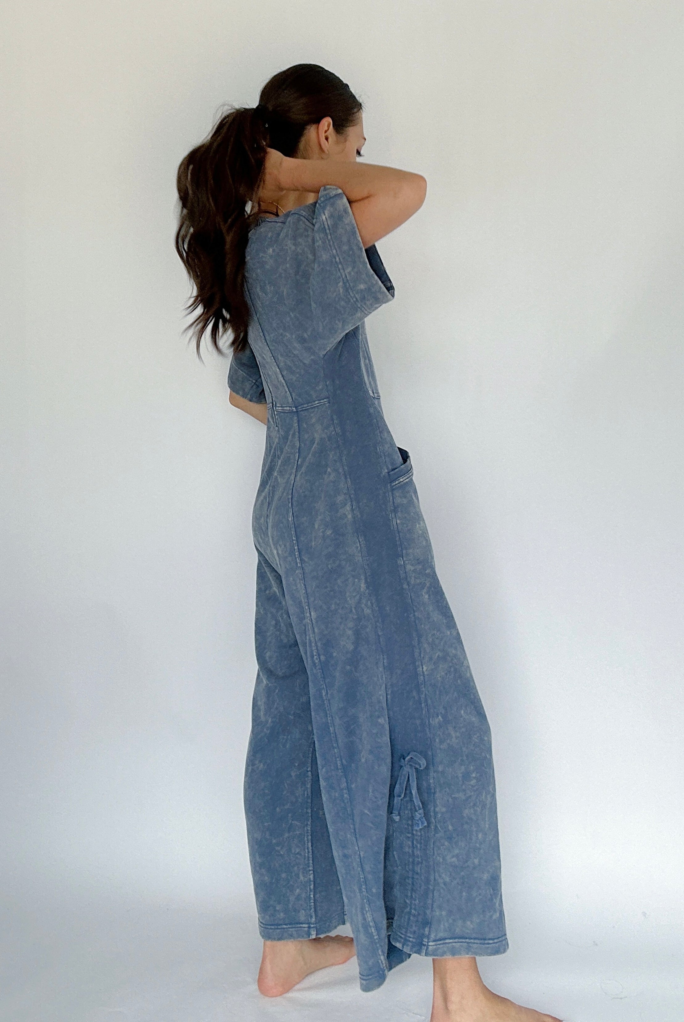 Woman wearing a blue mineral washed jumpsuit against a white background showing side view