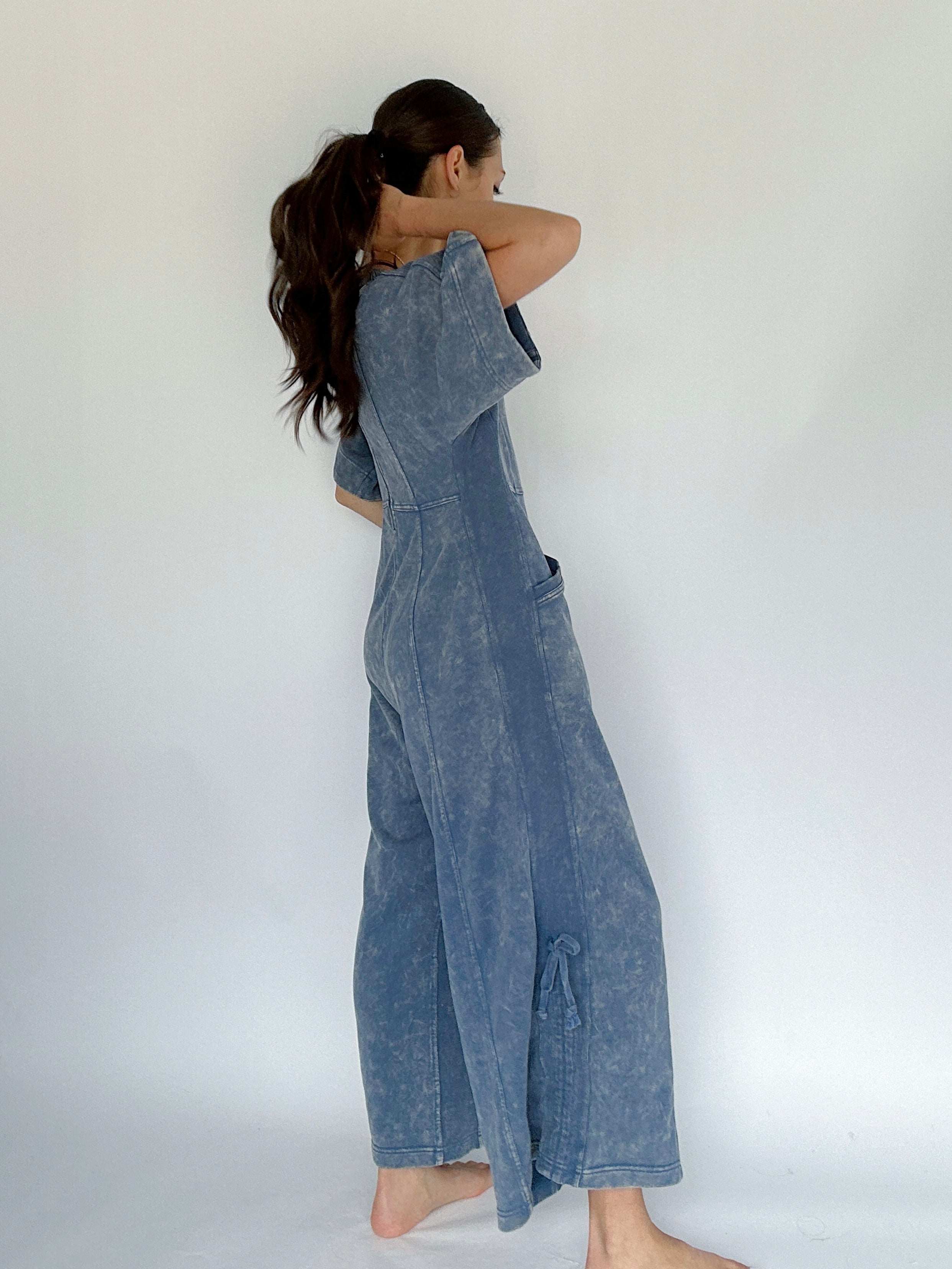 Woman wearing a blue mineral washed jumpsuit against a white background showing side view