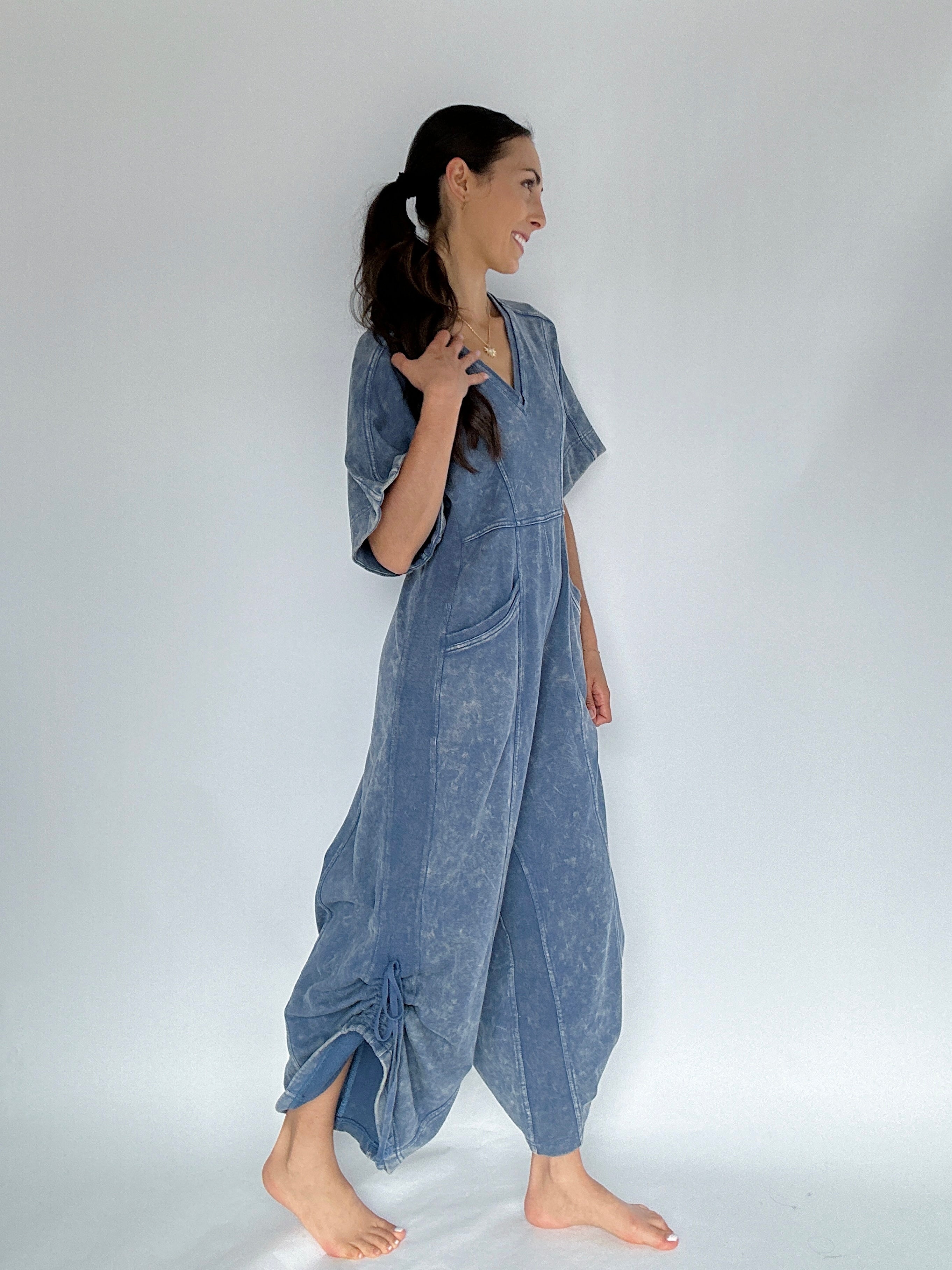 Woman wearing a blue jumpsuit against a white background to show side view