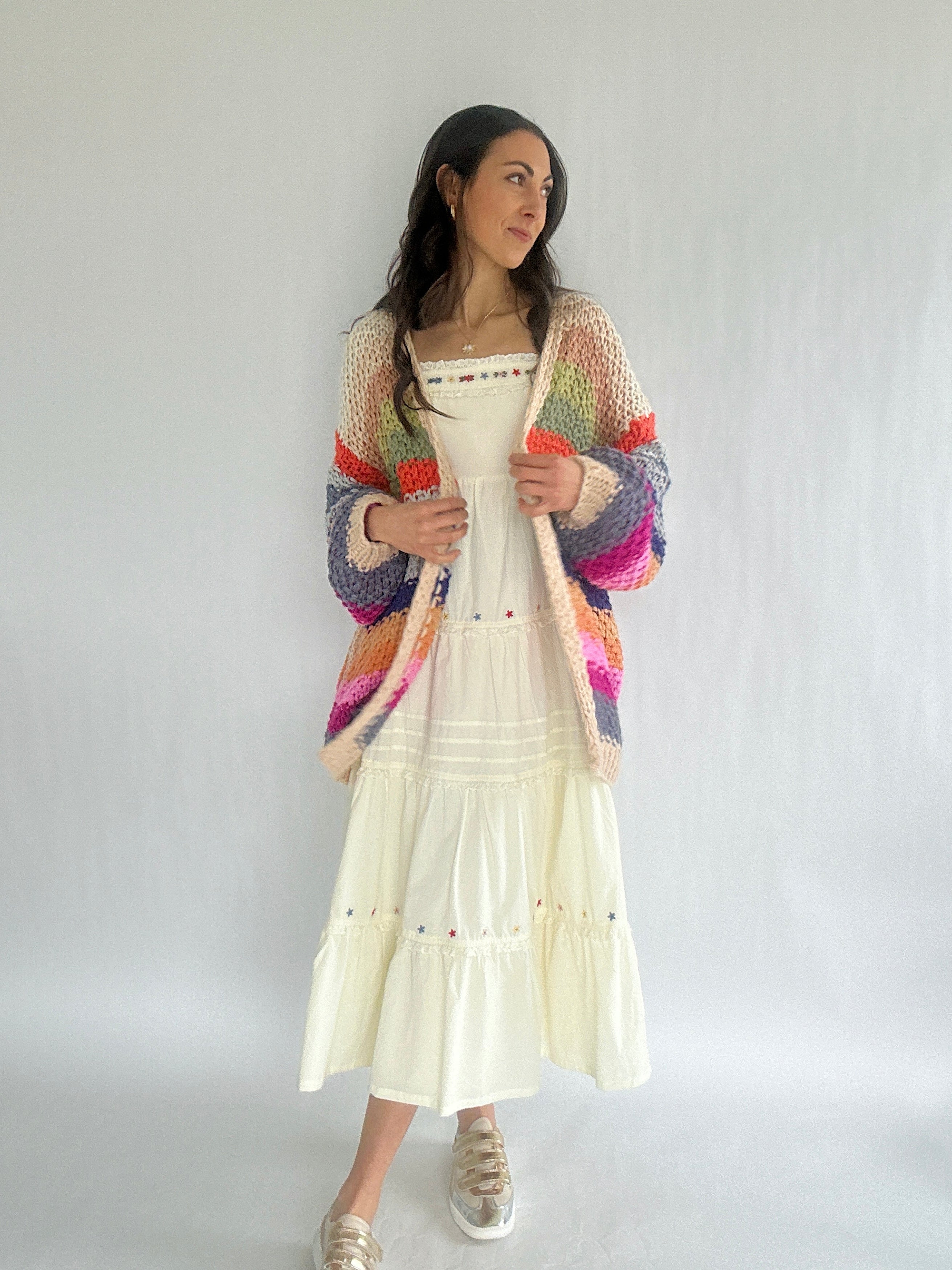Woman wearing a colorful cardigan over a white dress on a plain background
