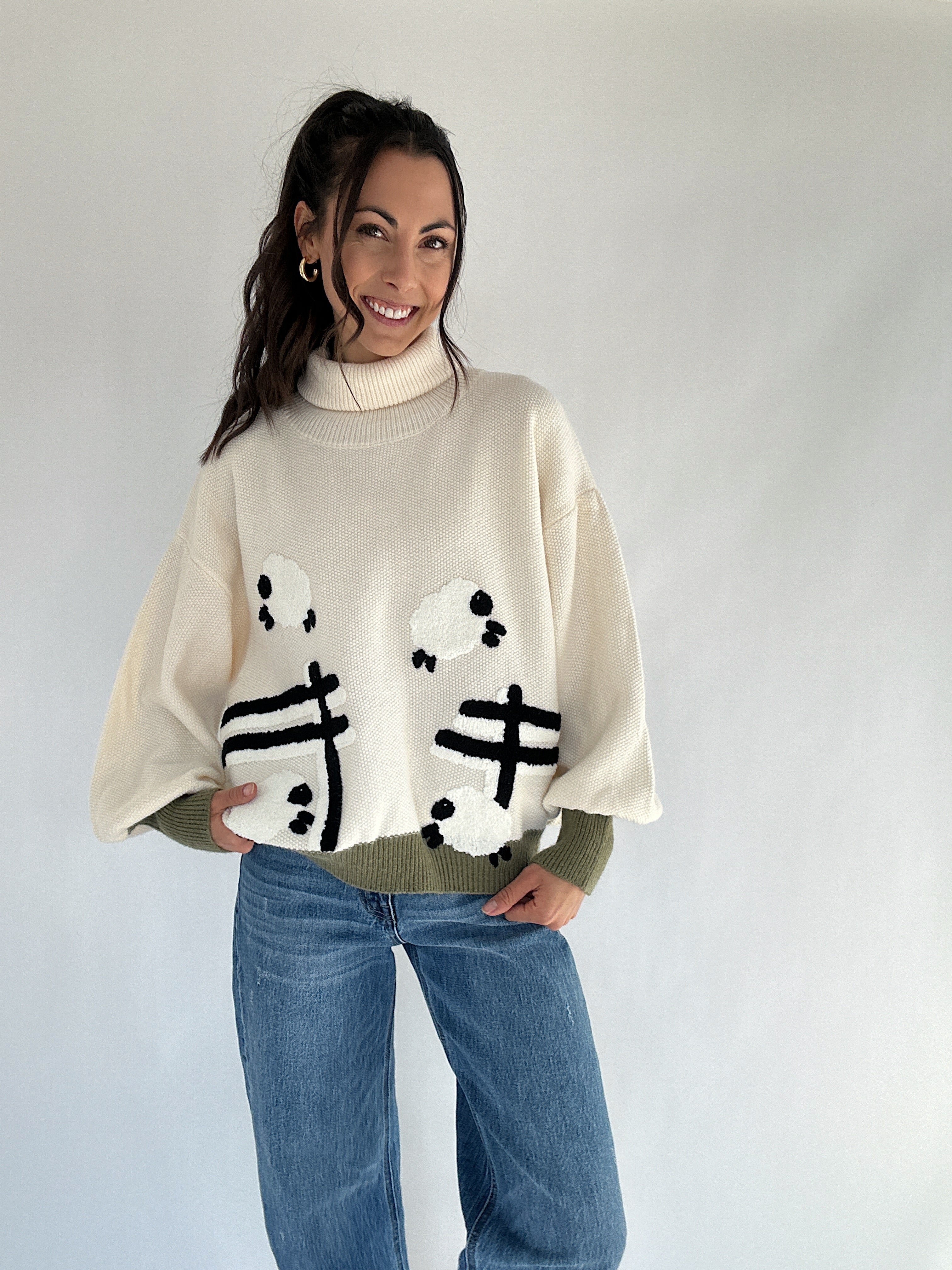 Woman wearing a cream turtle neck sweater with sheep jumping over a fence pattern on a plain background