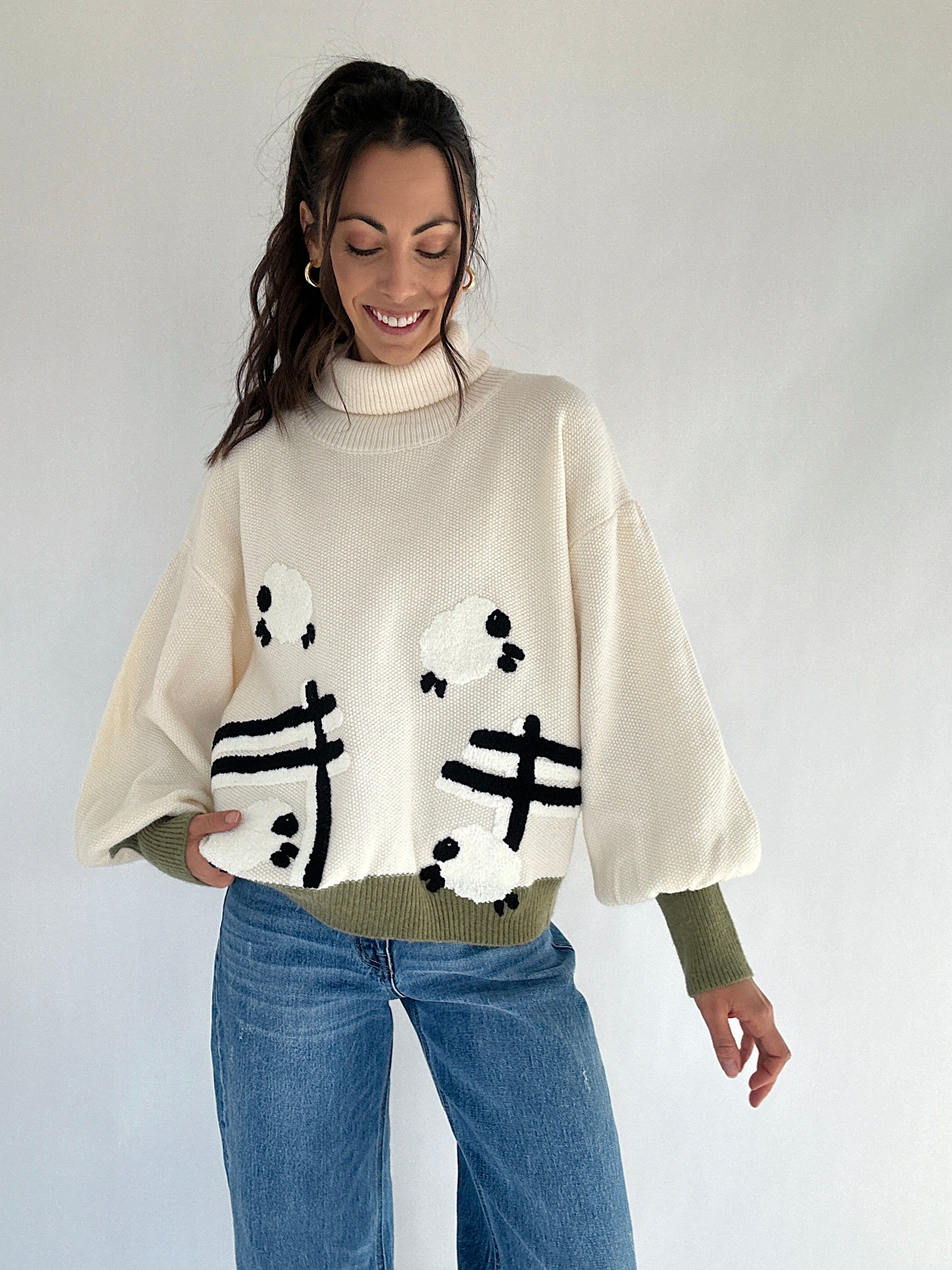 Woman wearing a cream sweater with sheep jumping over a fence patterns on a plain background