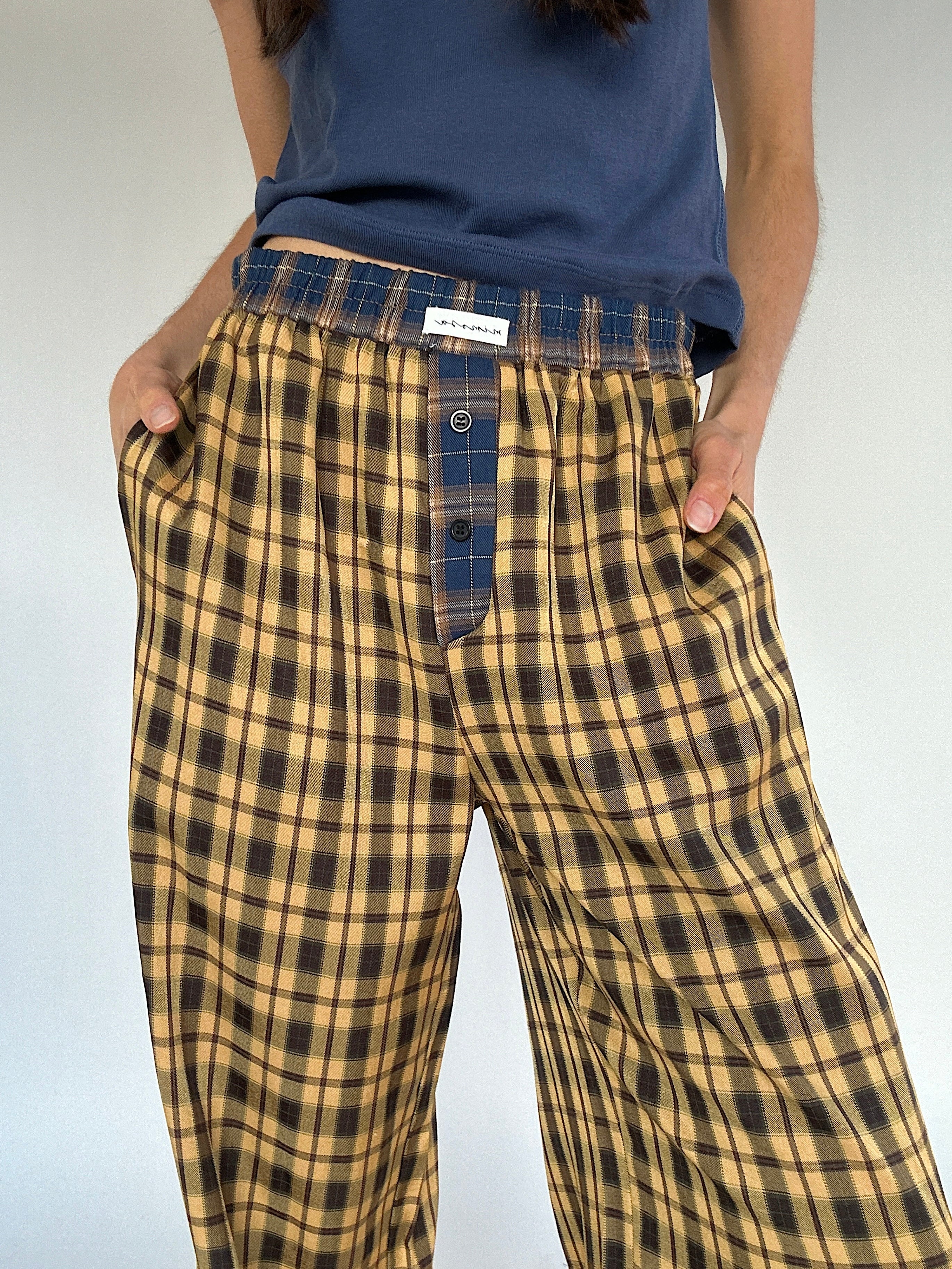 Person wearing mustard yellow plaid pants with a blue shirt on a plain background showing blue plaid waistband and side pockets