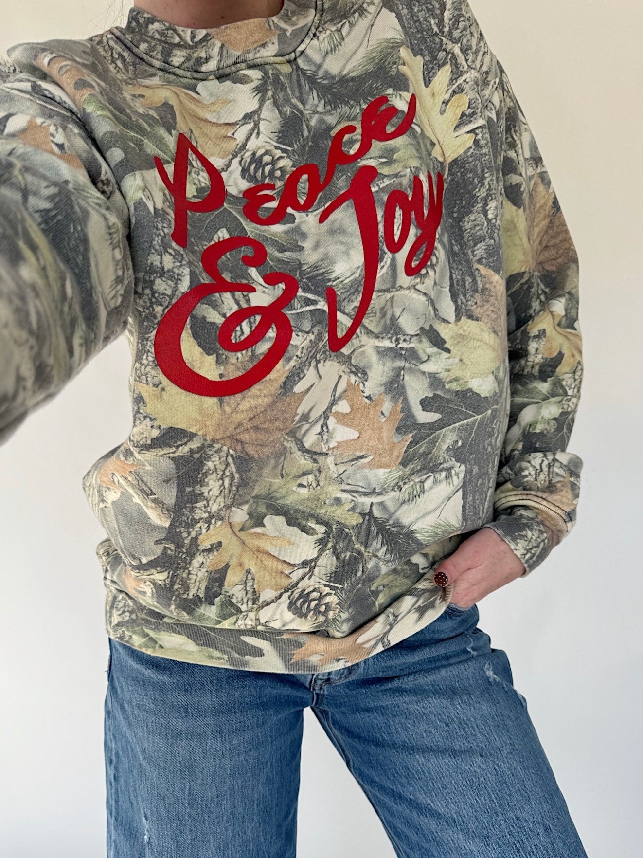 Camouflage hoodie with red text 'Peace & Love' worn by a person on a white background