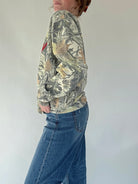 Person wearing a camouflage hoodie and blue jeans against a white background showing side