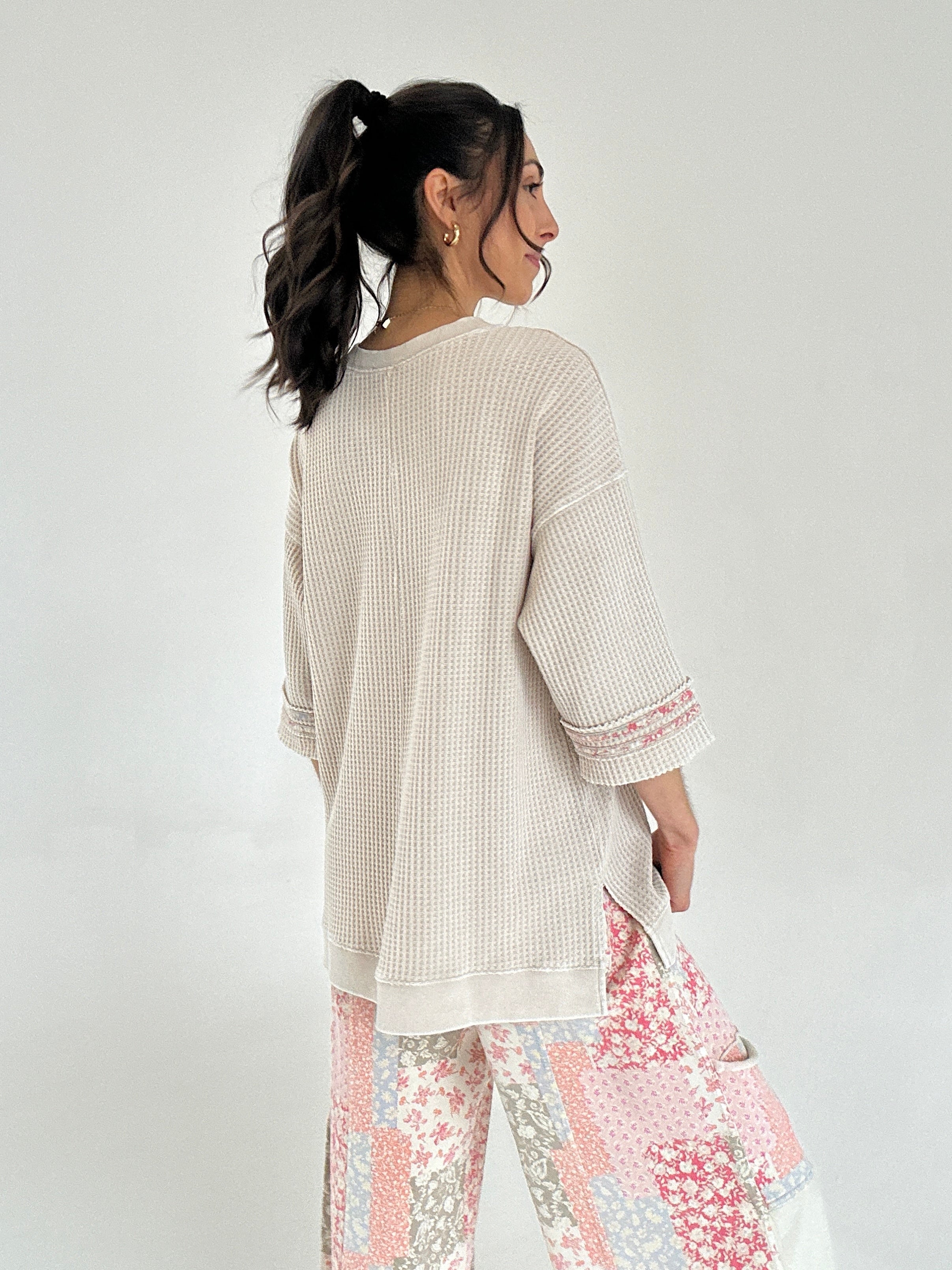 Woman wearing a beige textured top and floral pants on a plain background showing back