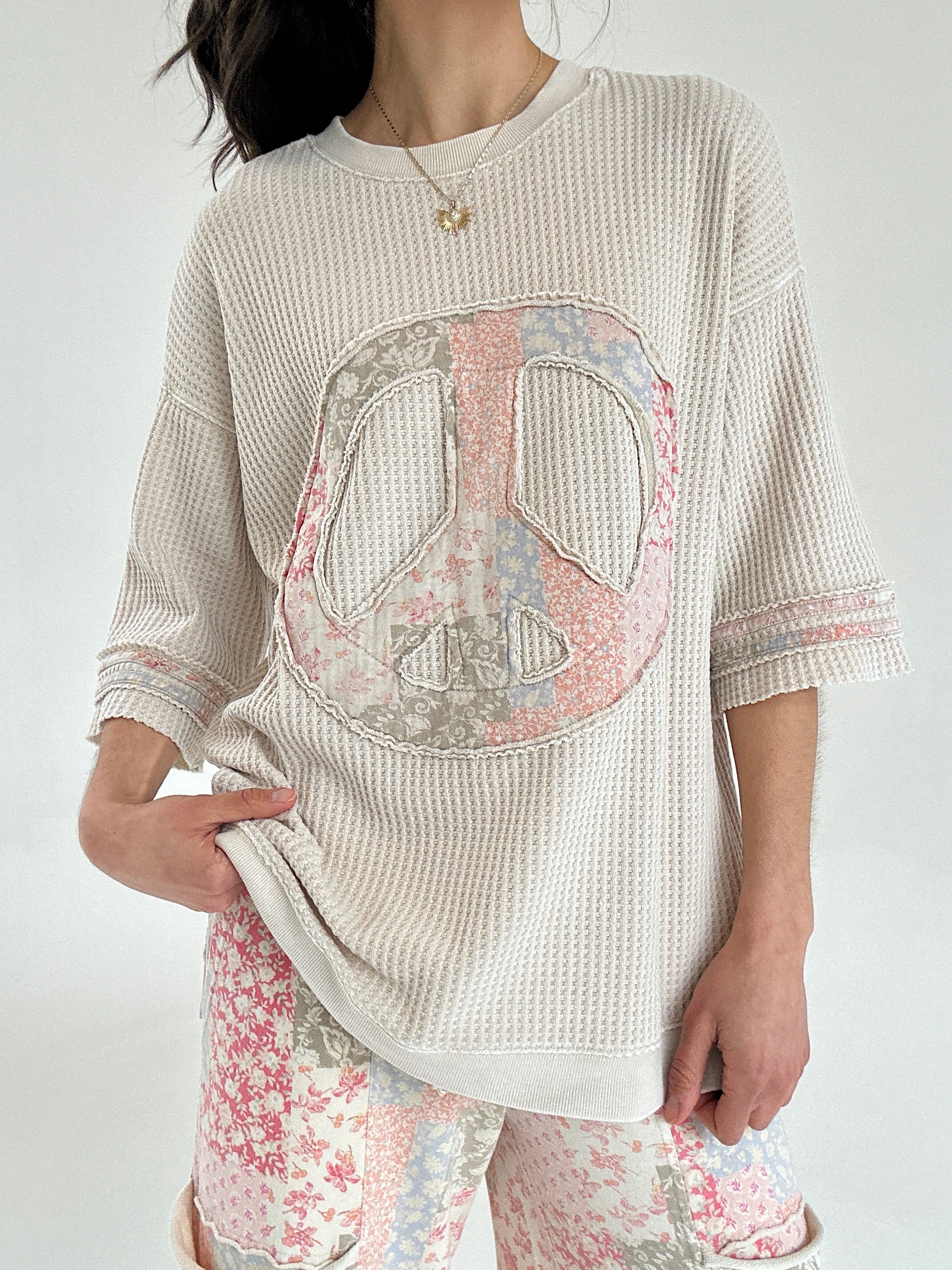 Person wearing a beige thermal knit top with a peace symbol design on a white background