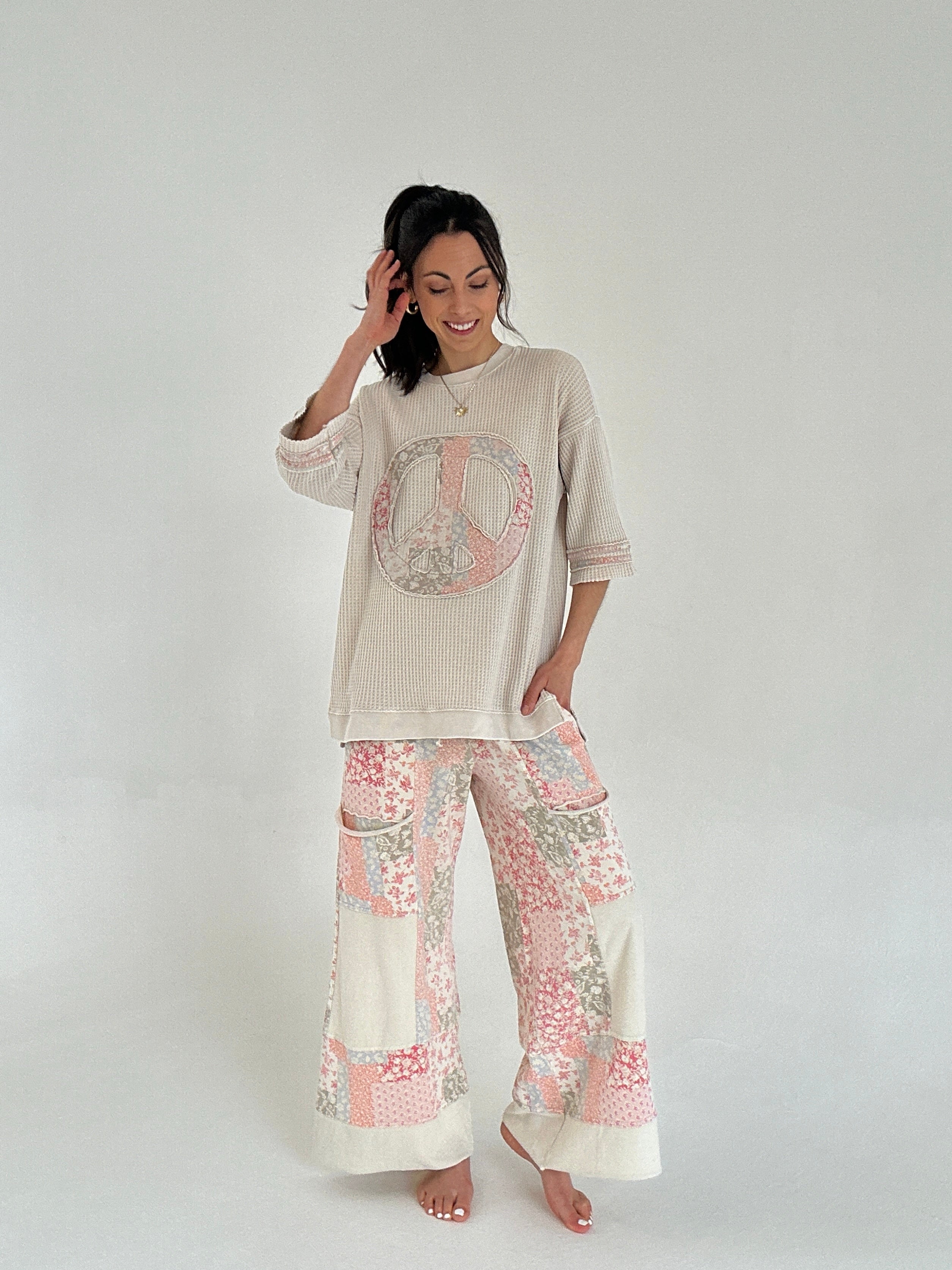 Woman wearing a beige peace sign top and floral pants on a white background