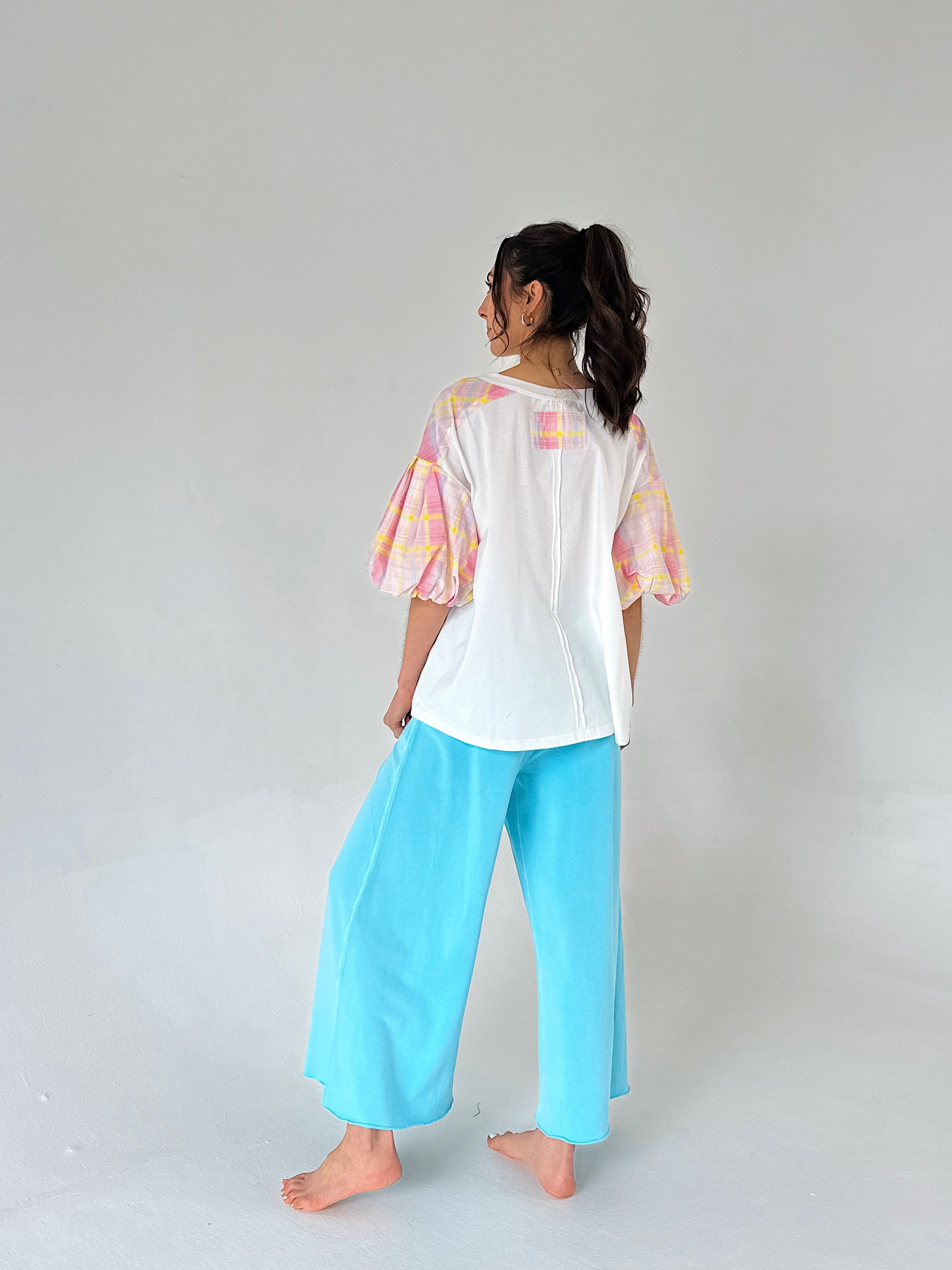 Person wearing a white top with colorful plaid sleeves and light blue pants on a plain background