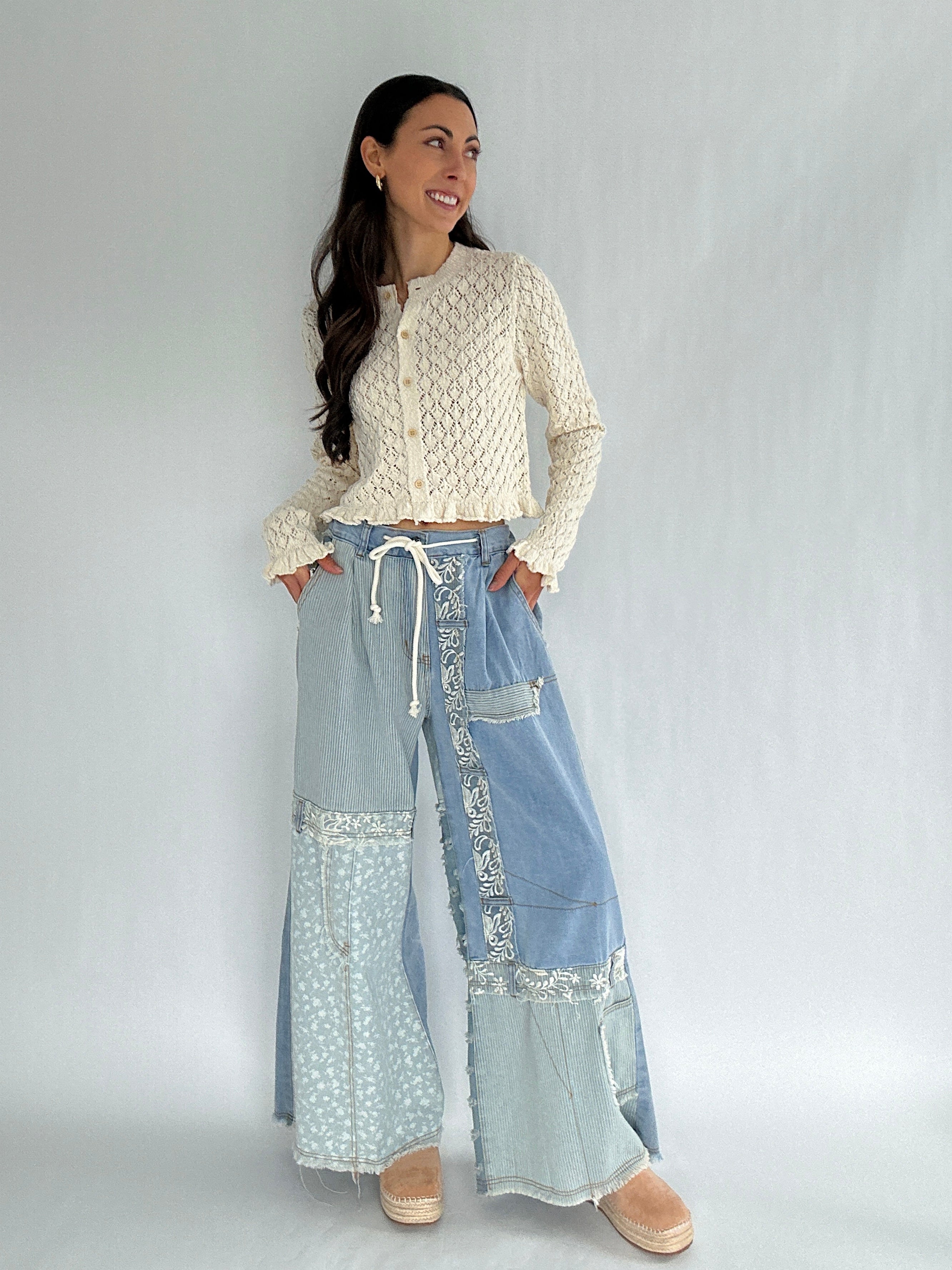Woman wearing a cream sweater and blue denim patchwork pants on a white background