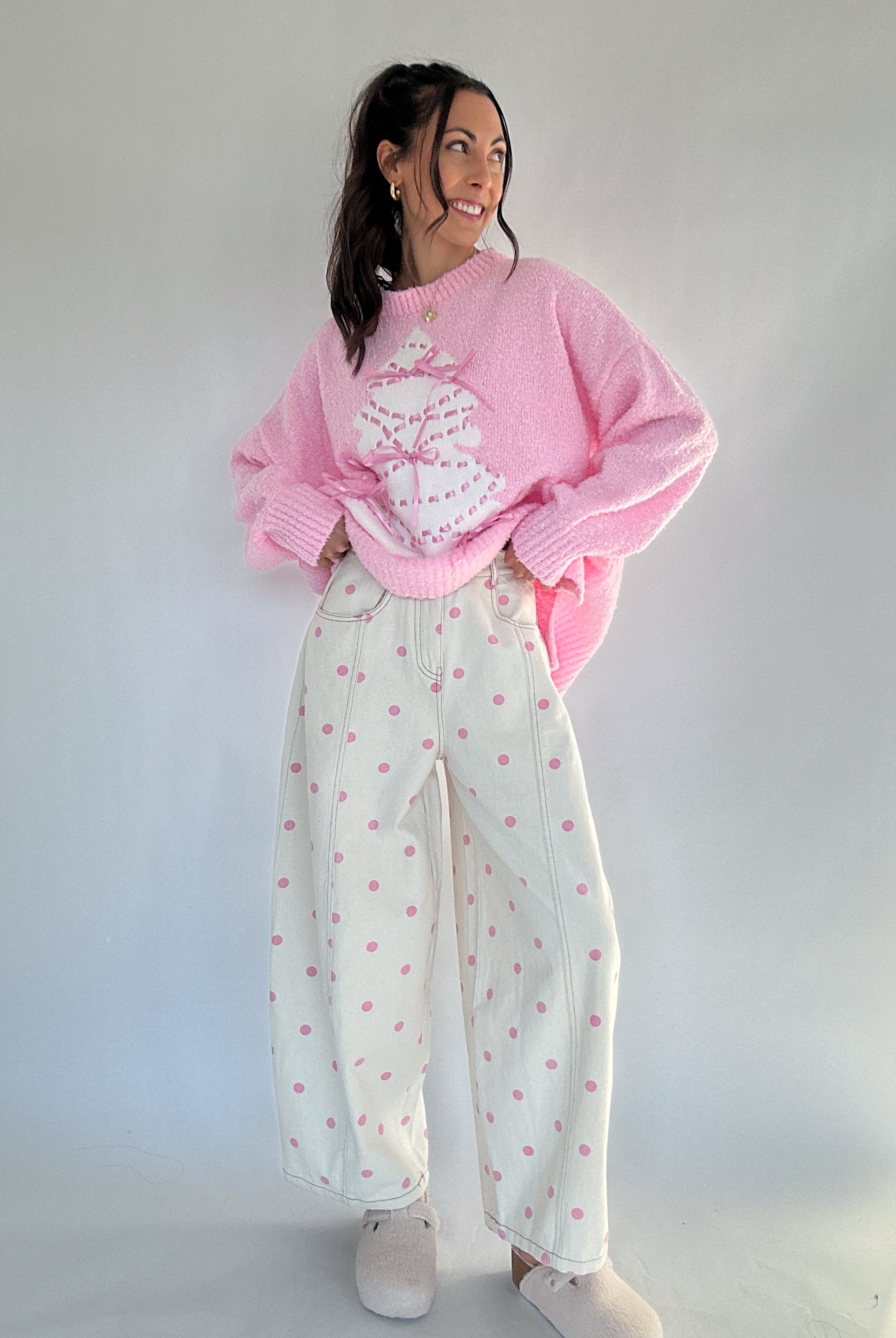 Person wearing a pink sweater and white pants with pink polka dots against a plain background
