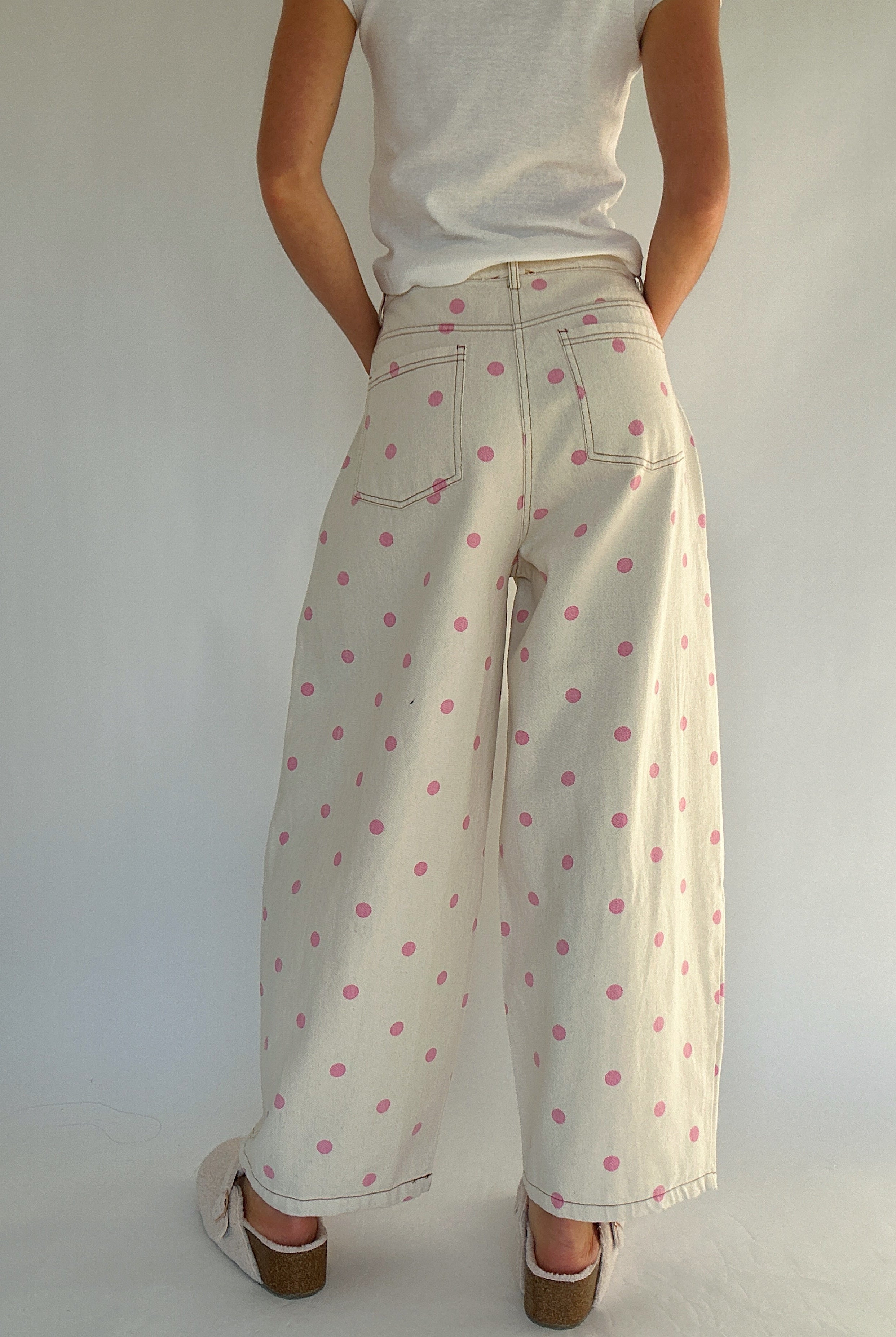 Person wearing a white top and beige pants with pink polka dots against a plain background