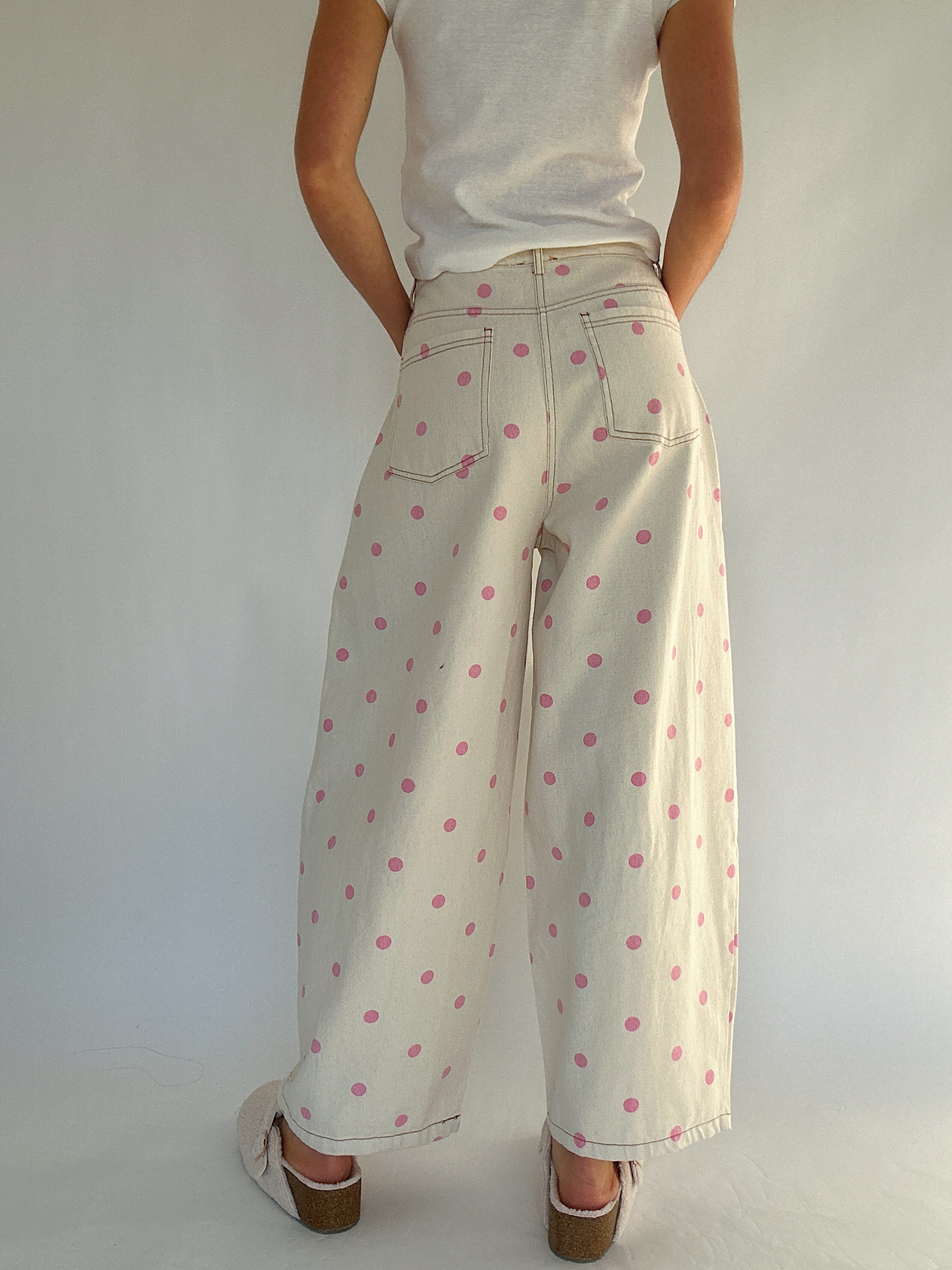 Person wearing a white top and beige pants with pink polka dots against a plain background