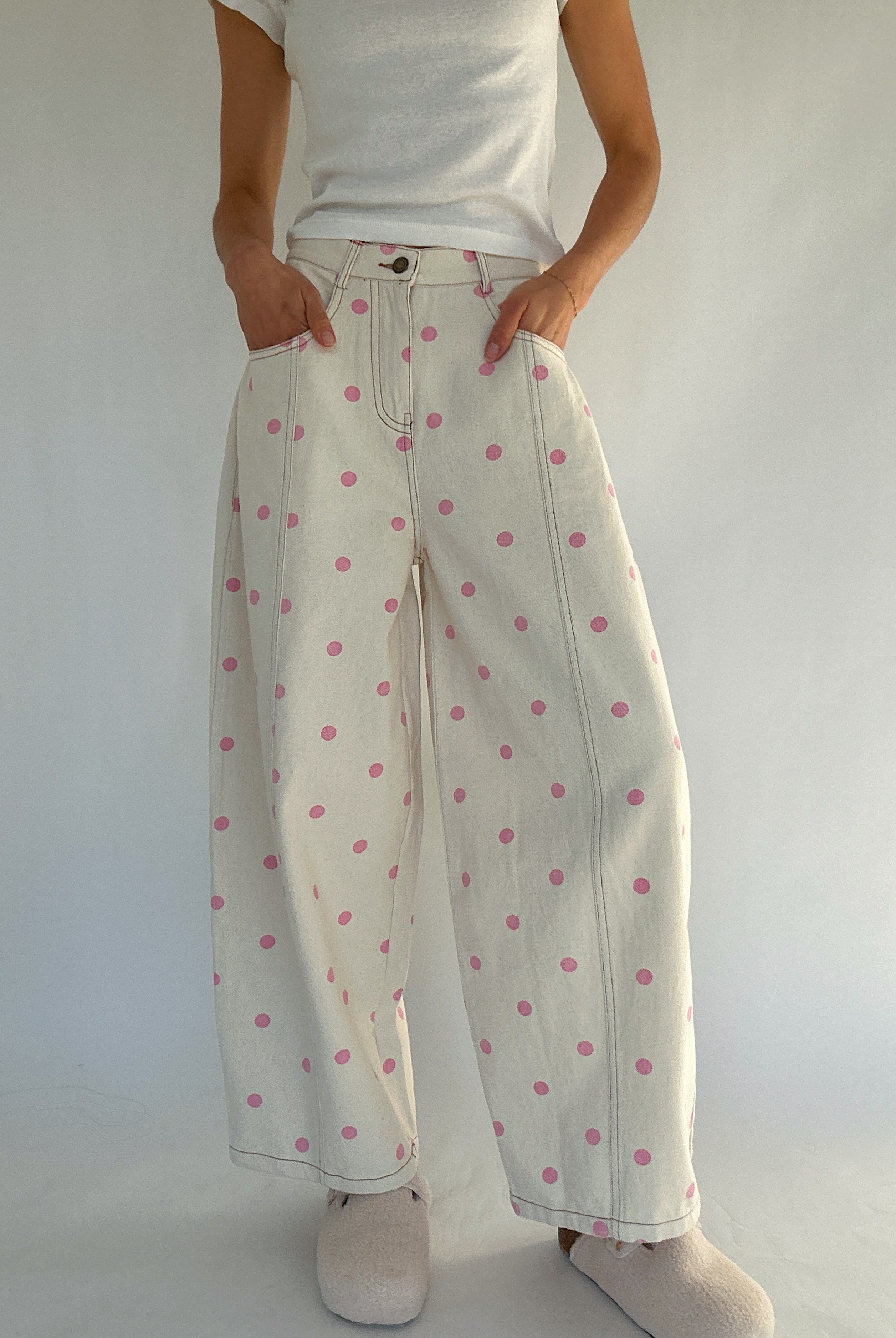 Person wearing white barrel pants with pink polka dots and a white shirt against a plain background