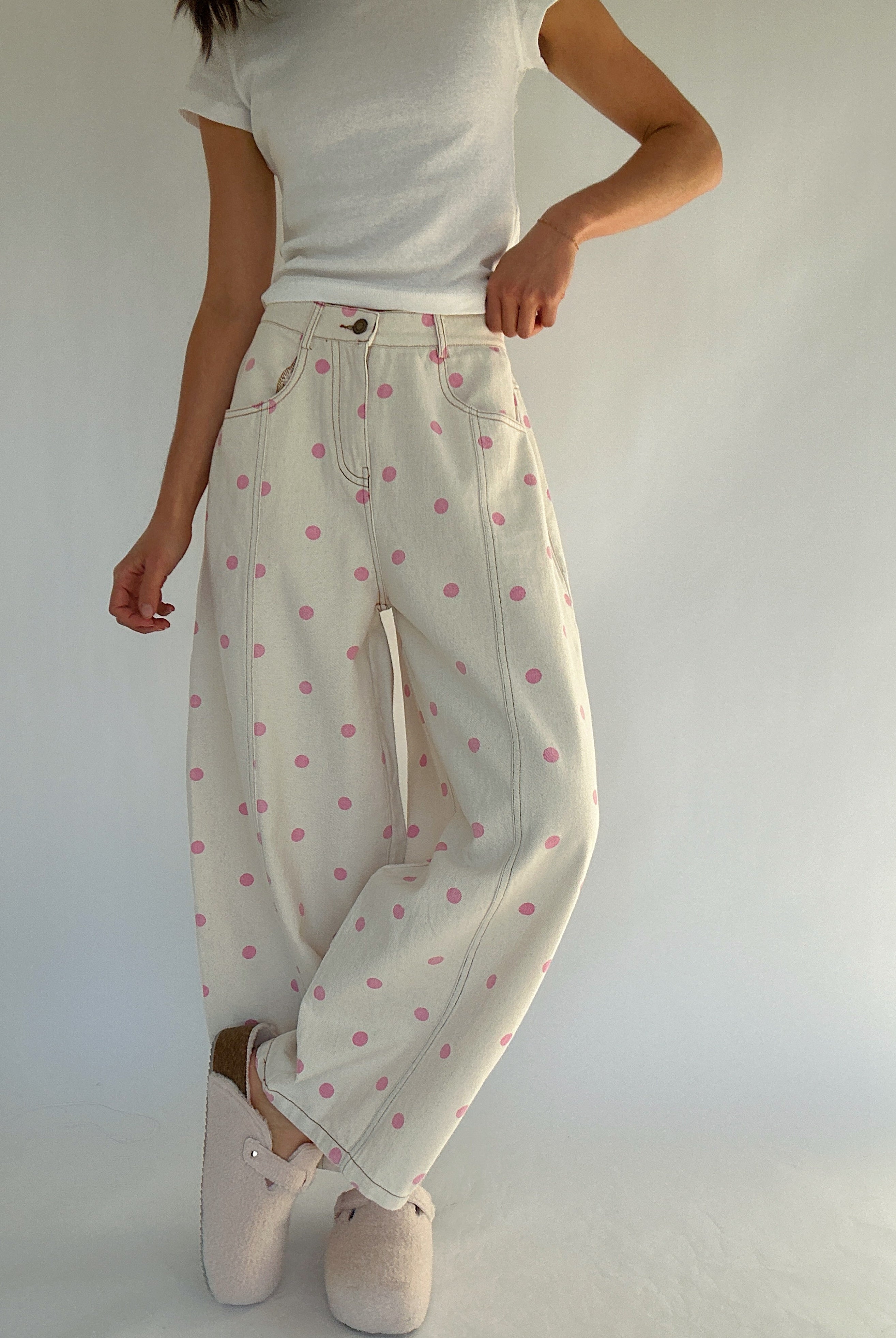 Person wearing white pants with pink polka dots and a white top against a plain background