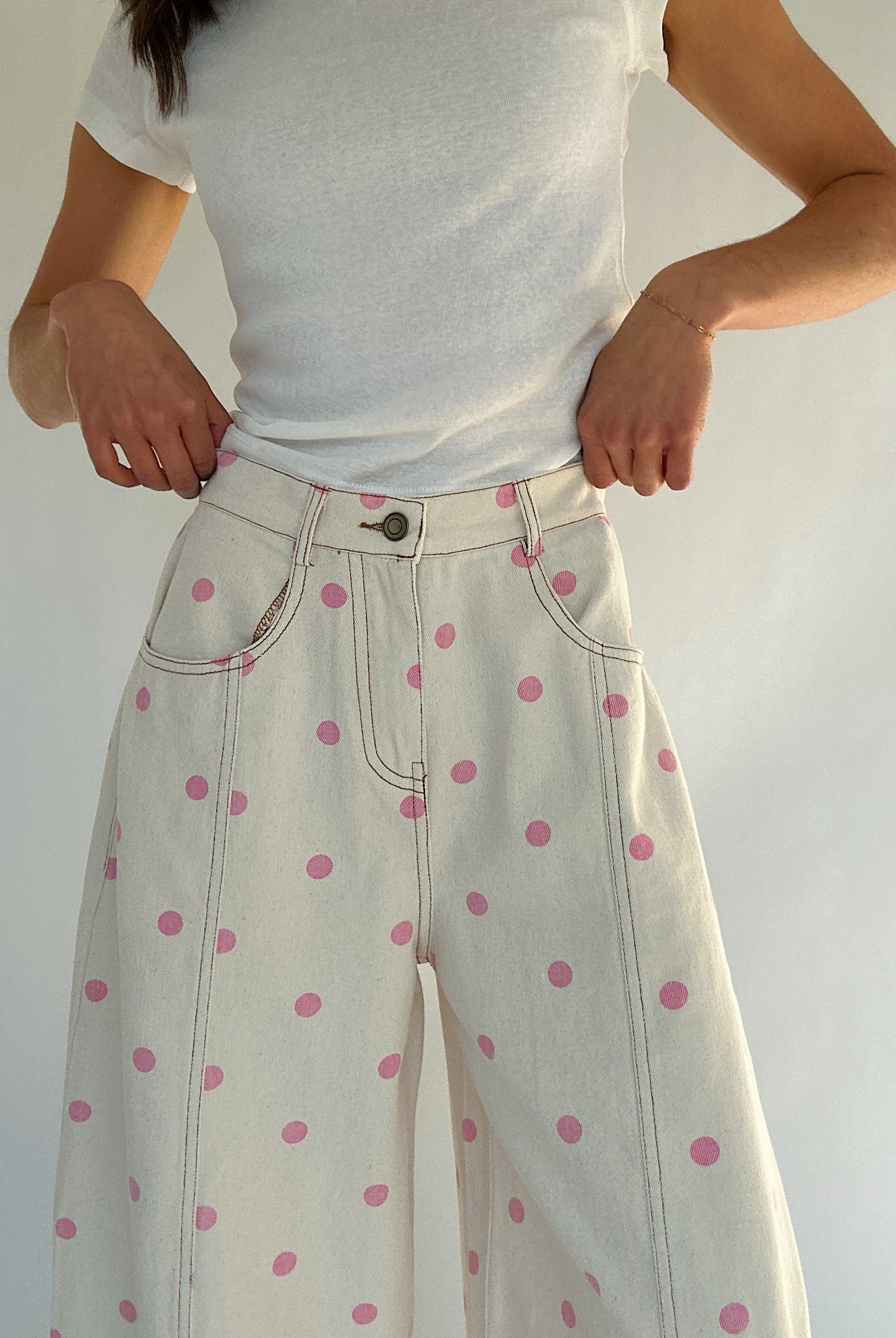 Person wearing a white t-shirt and white pants with pink polka dots against a plain background showing button and zip fly