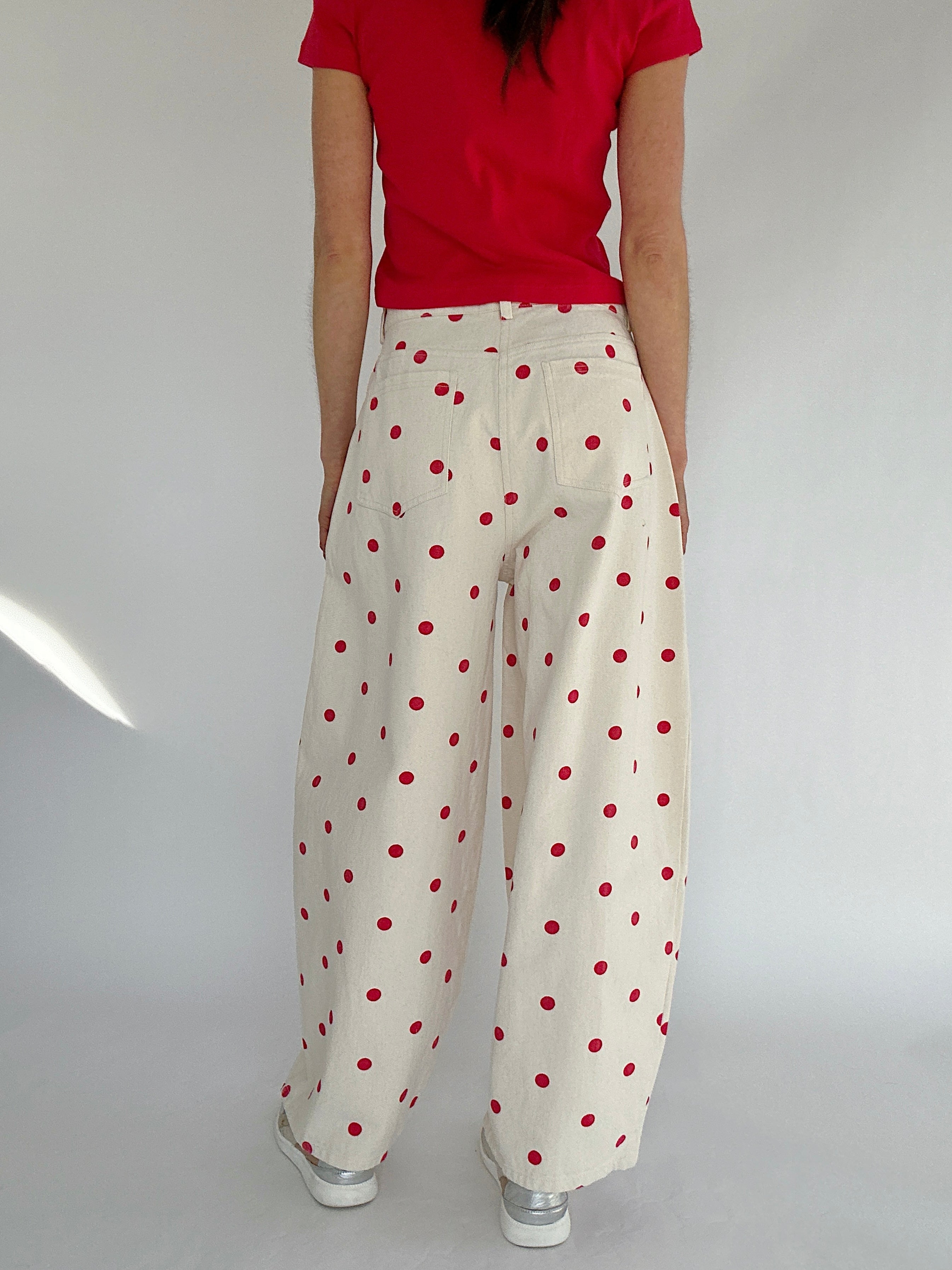 Person wearing a red top and white pants with red polka dots on a plain background from back