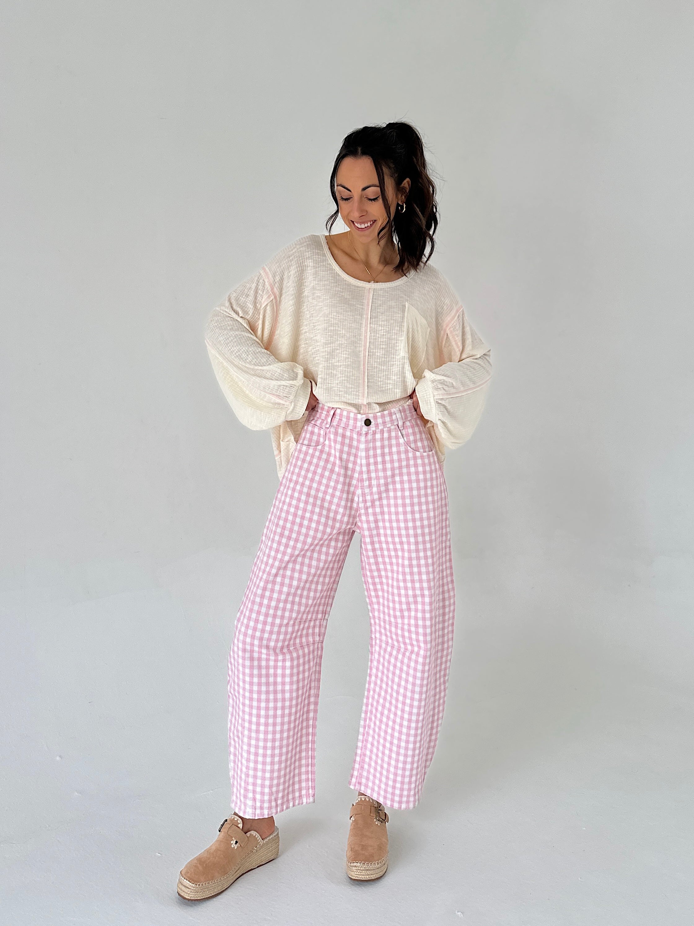 Woman wearing a cream sweater and pink checkered pants on a white background