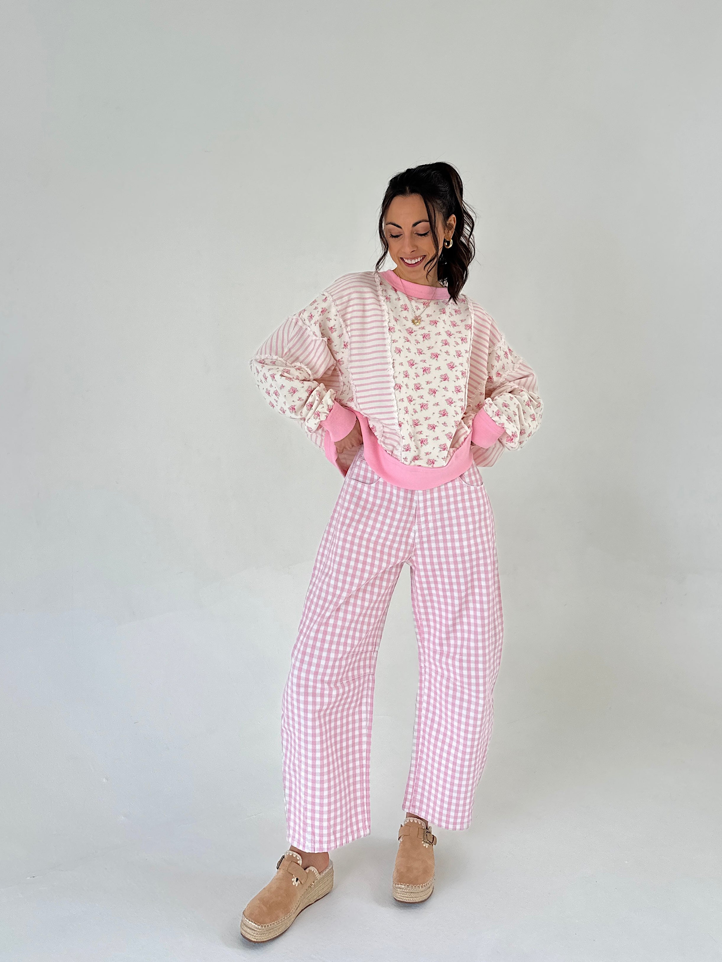 Person wearing a pink checkered pants with a floral striped top on a plain background