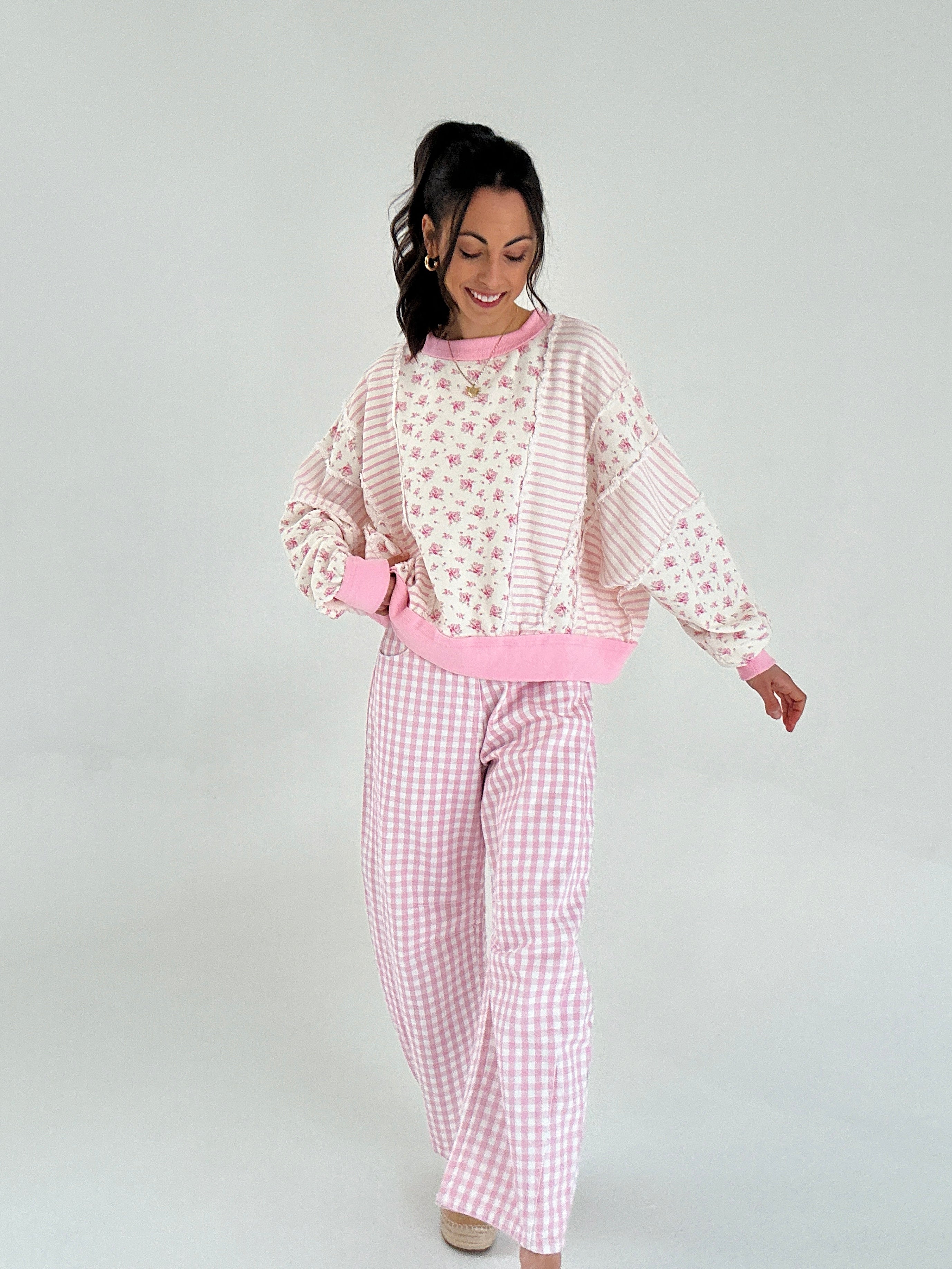 Woman wearing pink and white checkered pants and floral pullover on a plain background