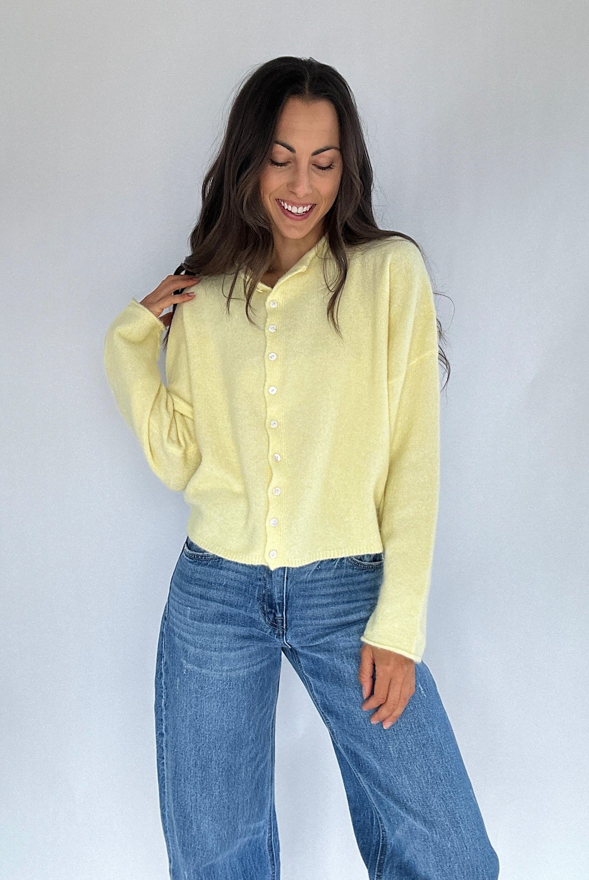 Woman wearing a light yellow shirt and blue jeans against a white background