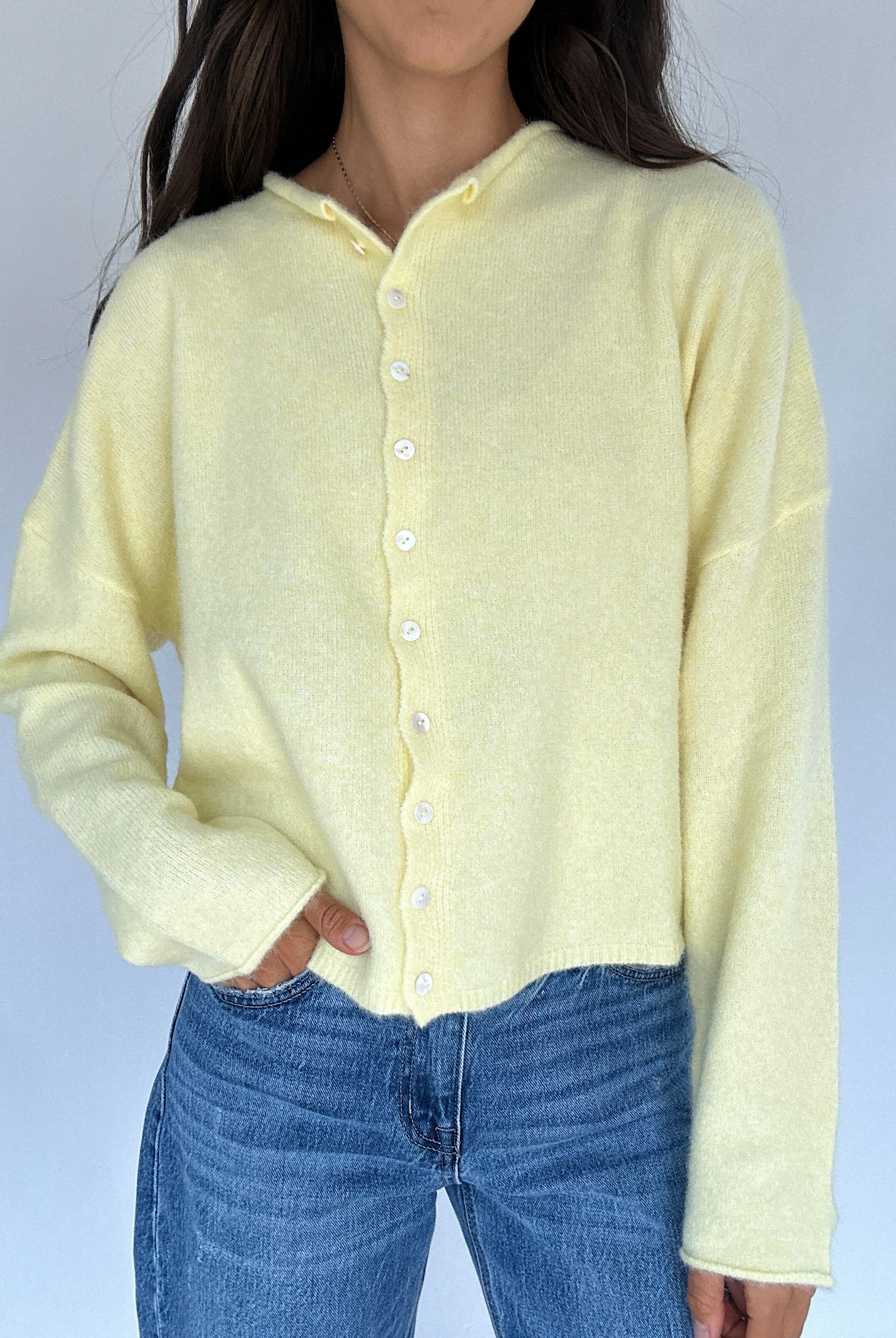 Person wearing a light yellow cardigan over a blue top against a plain background