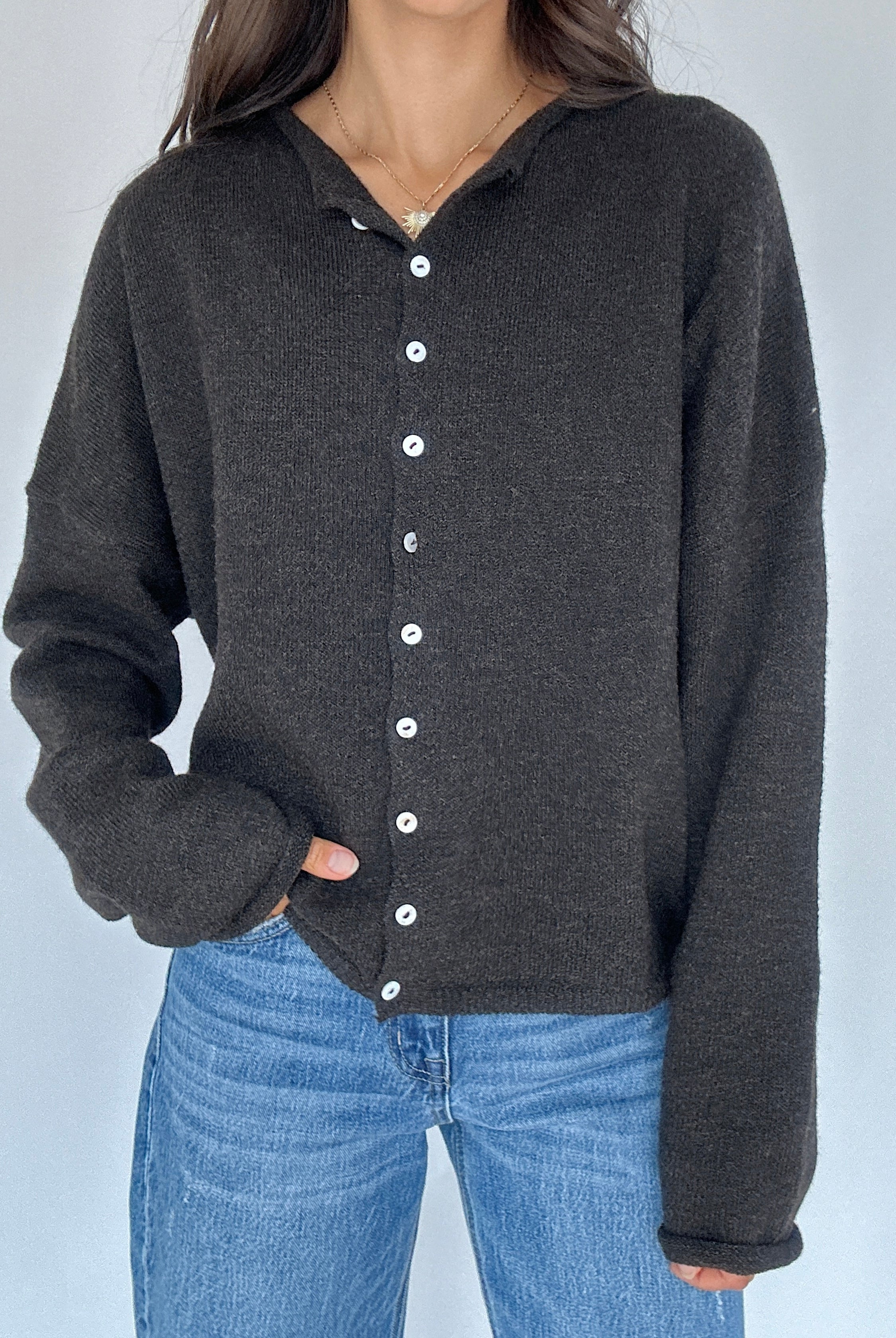 Person wearing a dark chocolate button-up cardigan over blue jeans against a light gray background