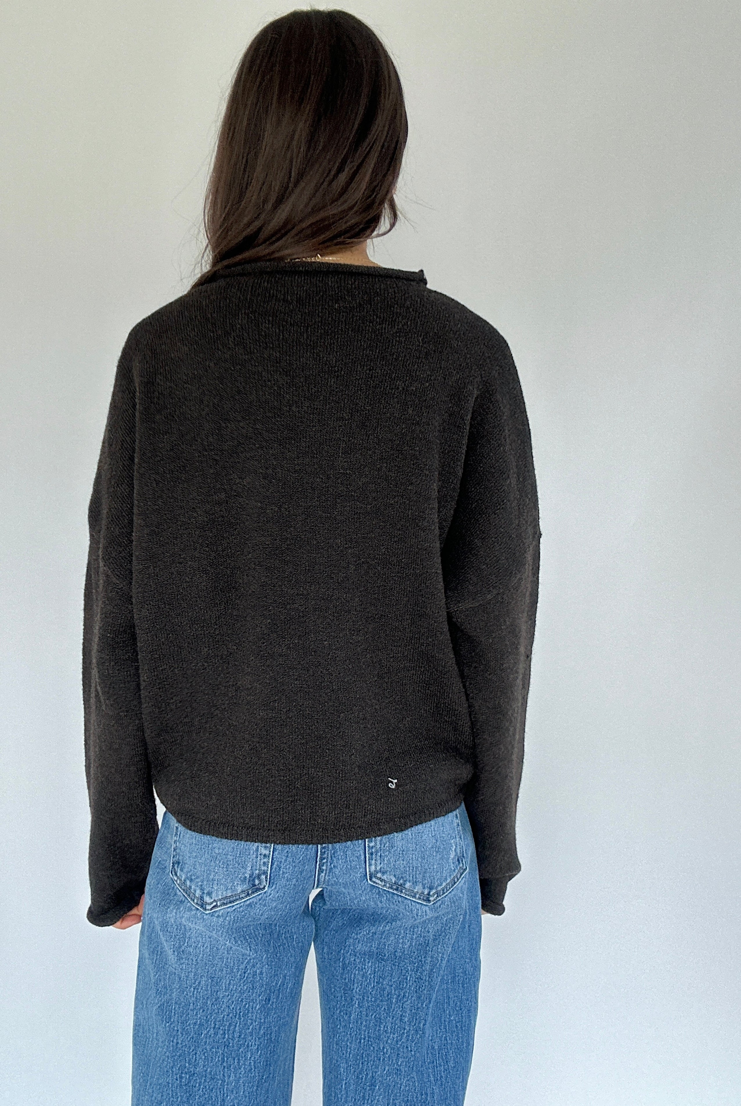 Person wearing a dark gray sweater and blue jeans against a white background