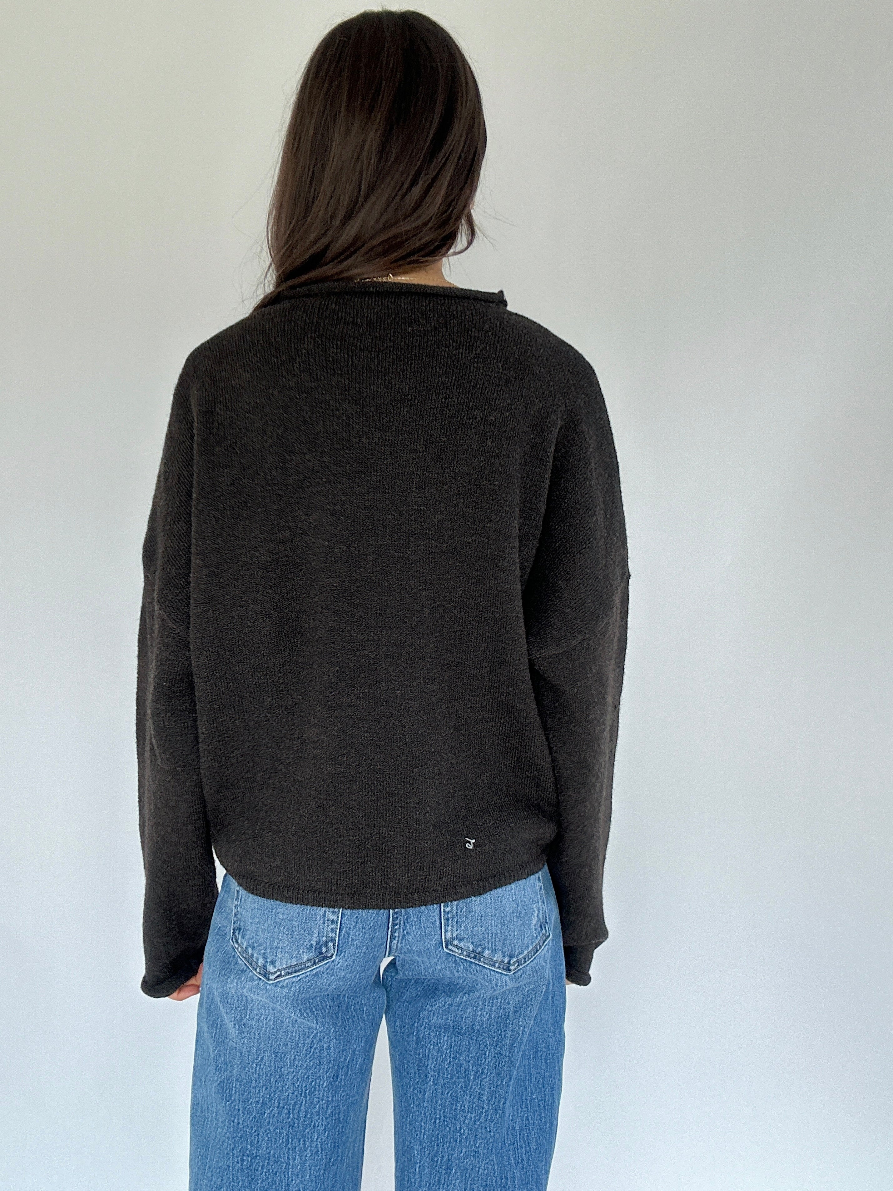 Person wearing a dark gray sweater and blue jeans against a white background