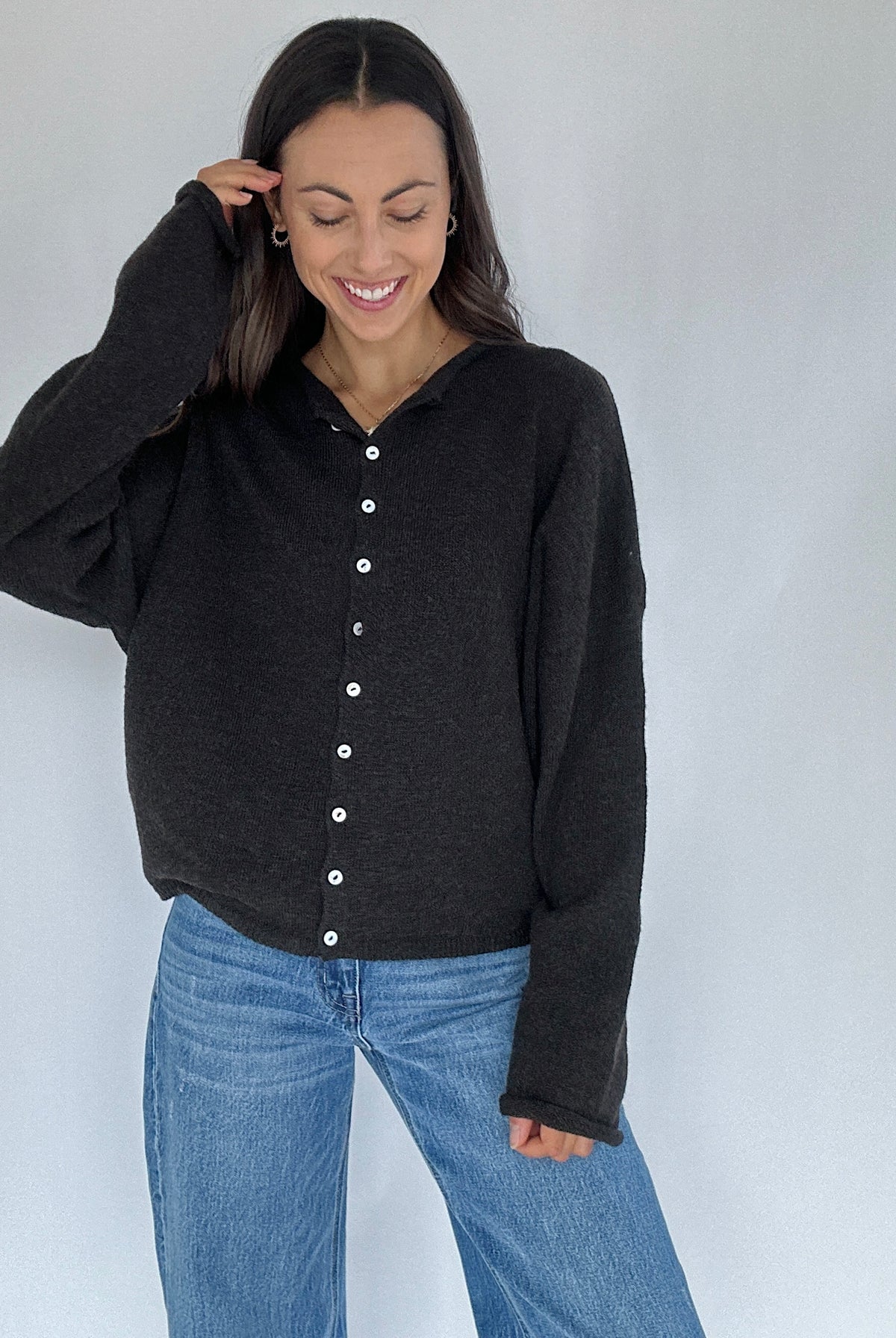 Woman wearing a black cardigan and blue jeans against a white background