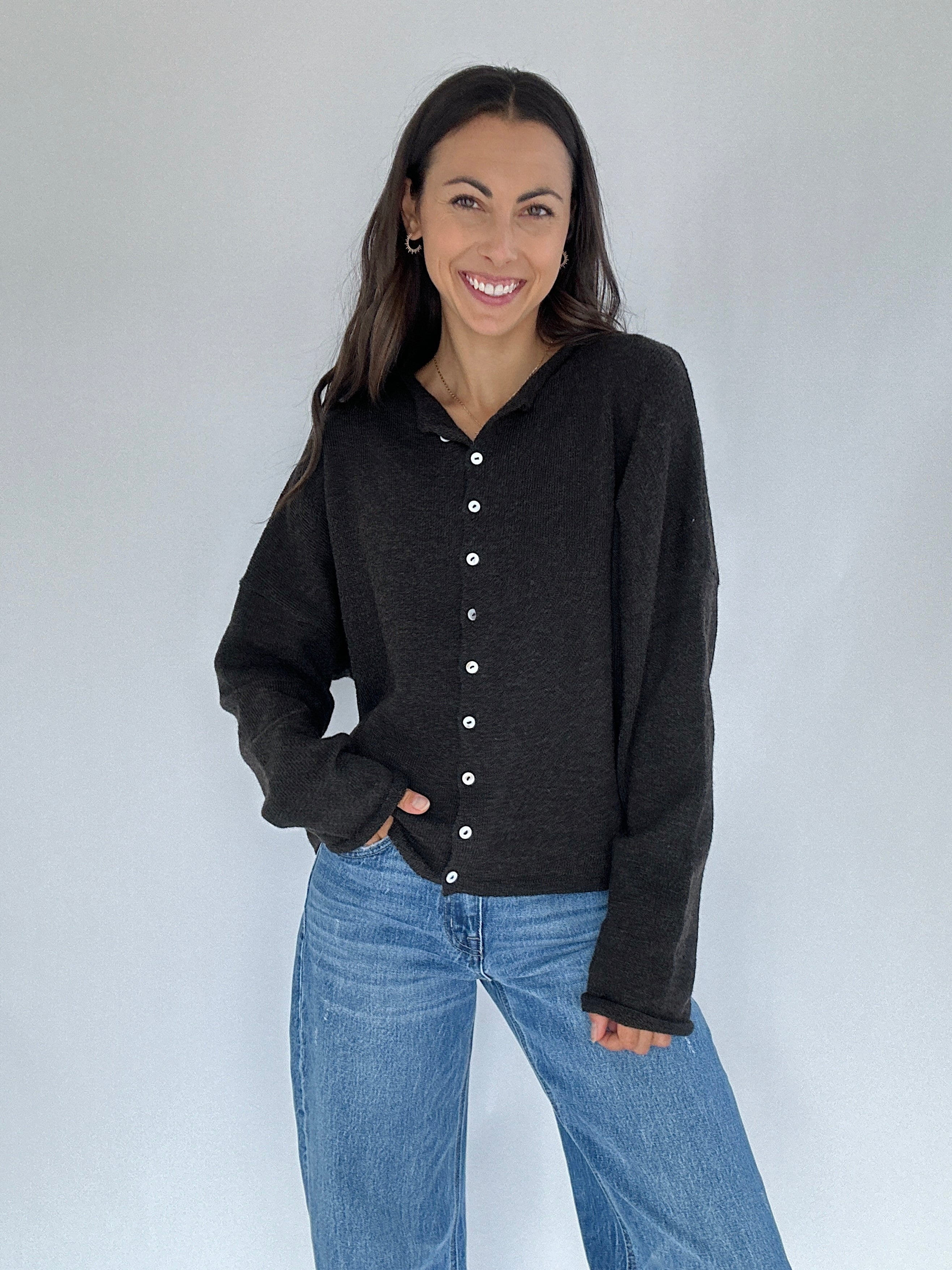 Woman wearing a chocolate button-up cardigan and blue jeans against a white background