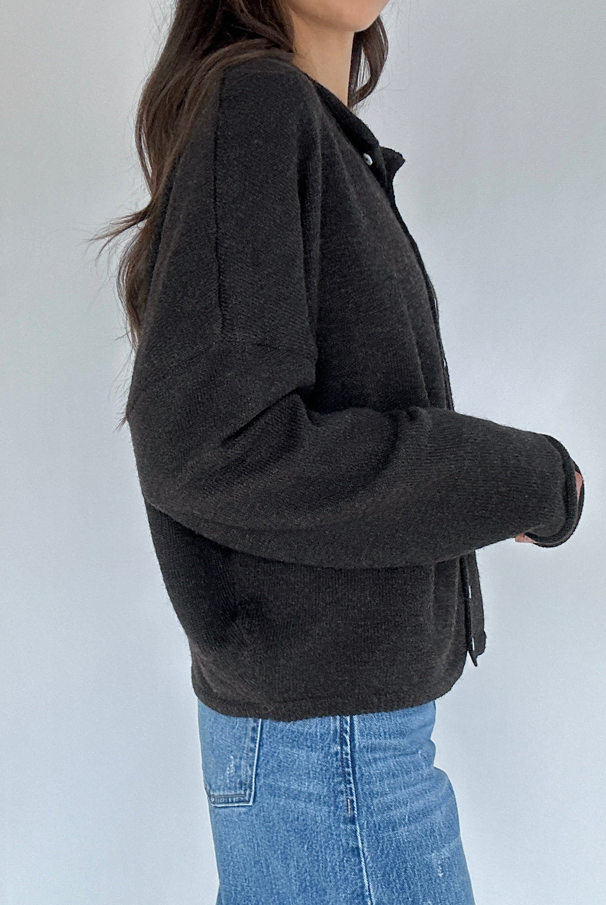 Person wearing a dark gray cardigan and blue jeans against a white background