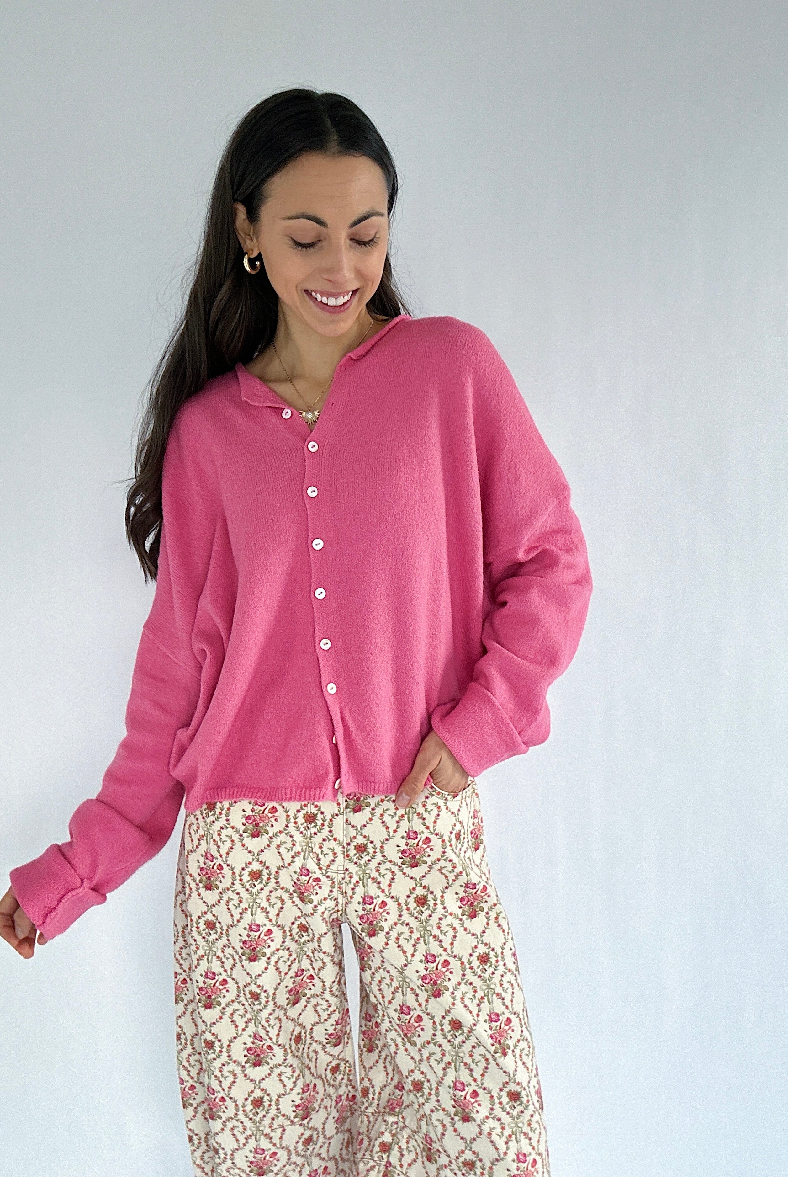 Woman wearing a pink cardigan with floral patterned pants against a white background