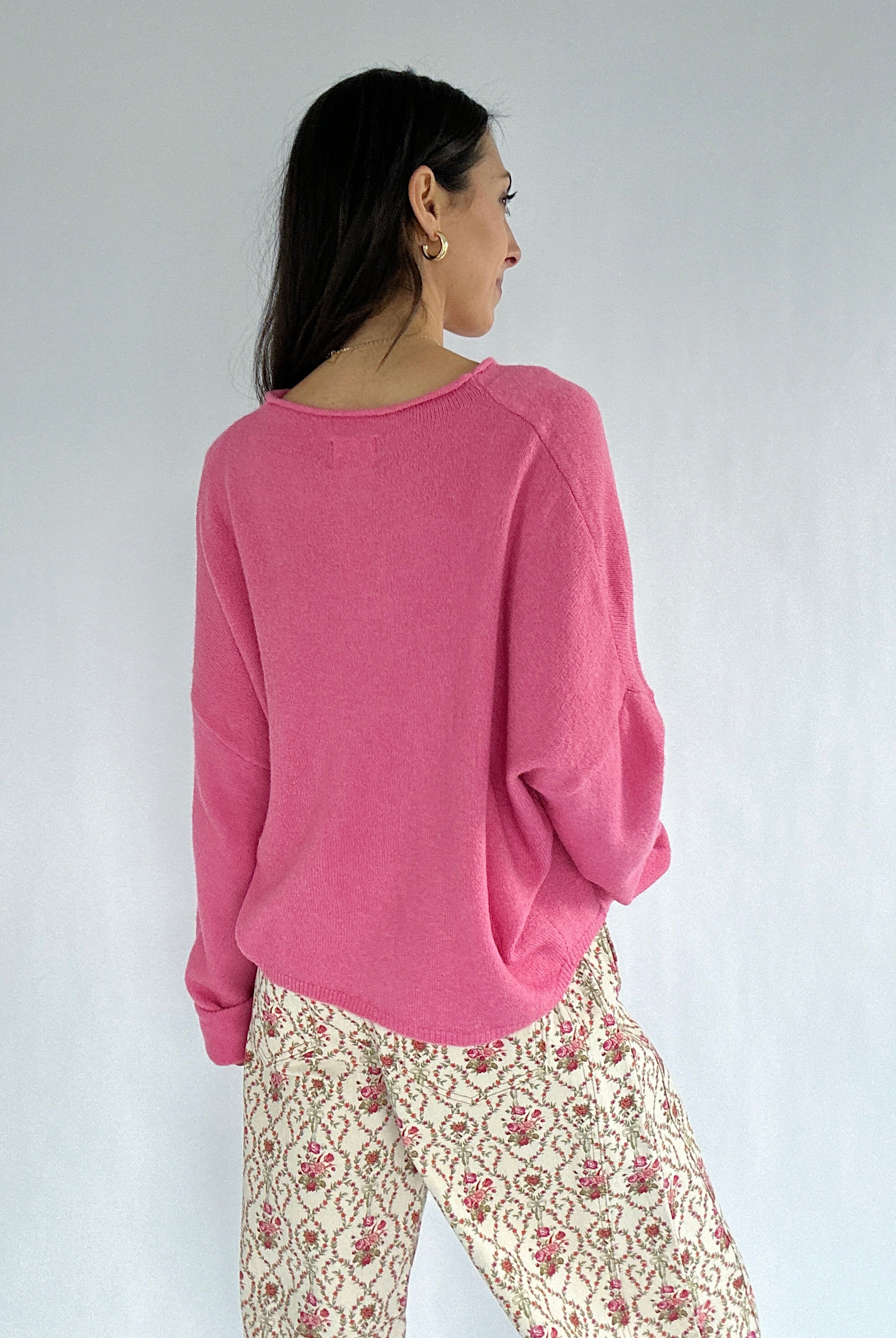 Woman wearing a pink sweater and patterned pants against a white background showing the back