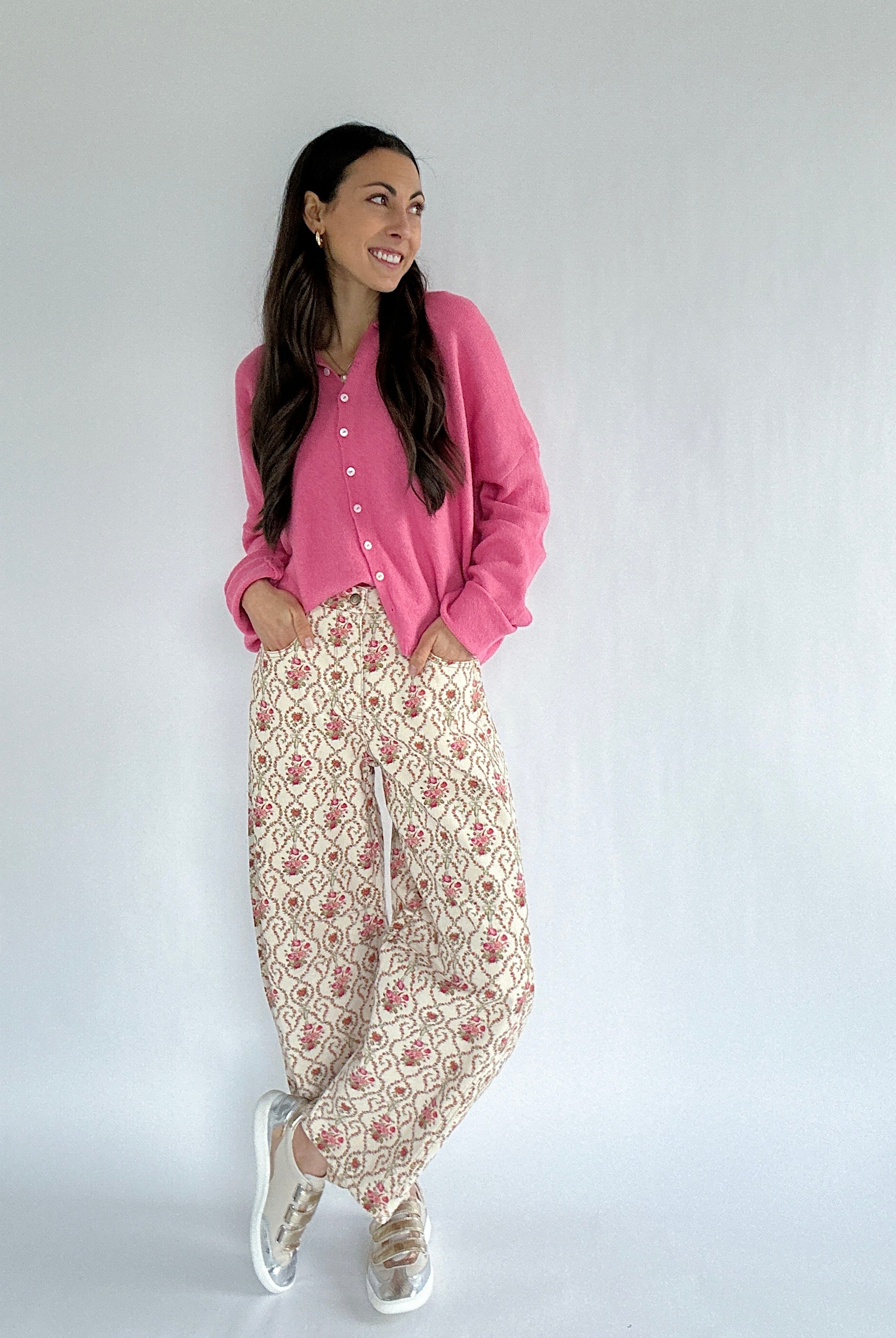 Woman wearing a pink cardigan and floral pants against a white background