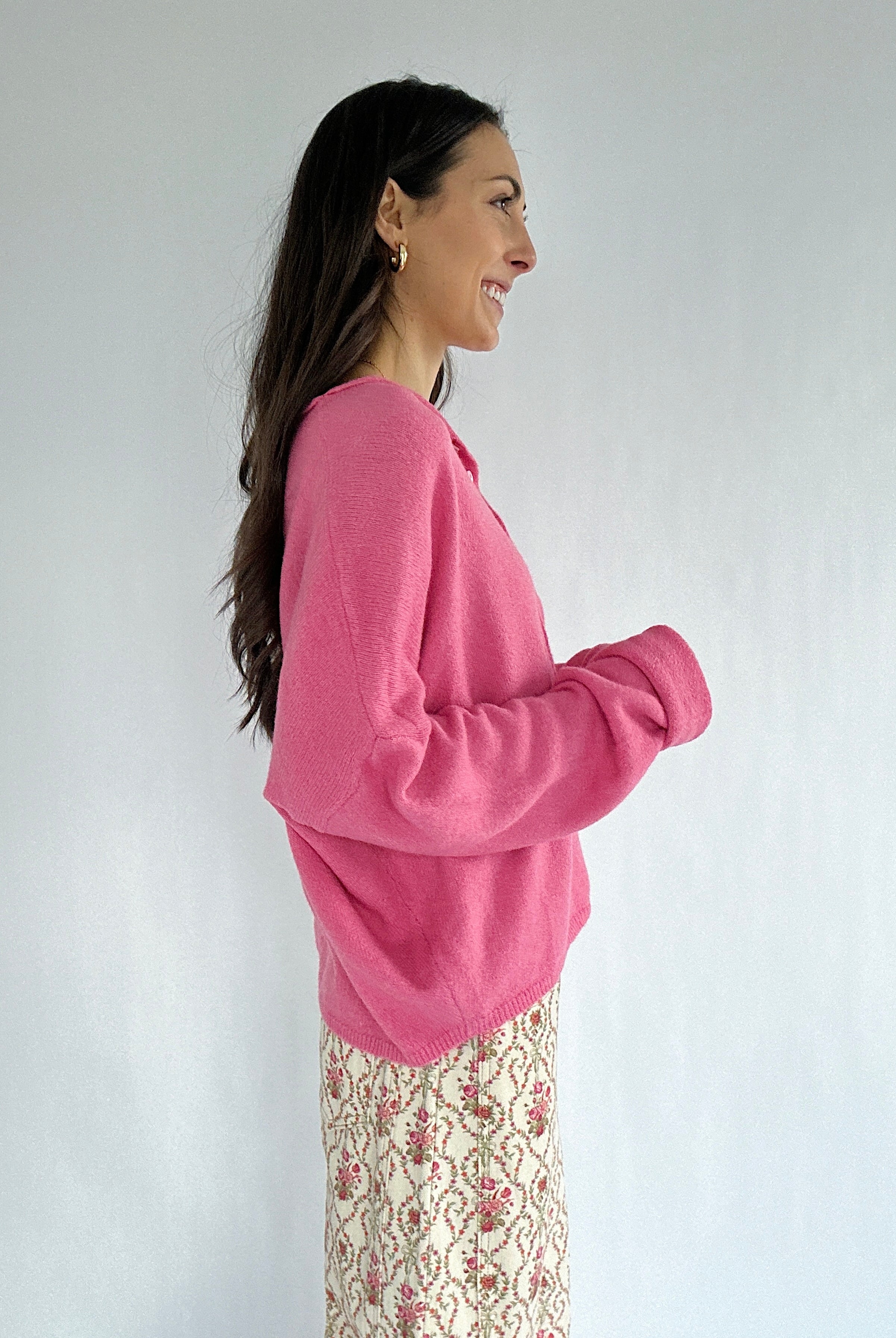 Woman wearing a pink sweater against a white background showing the side
