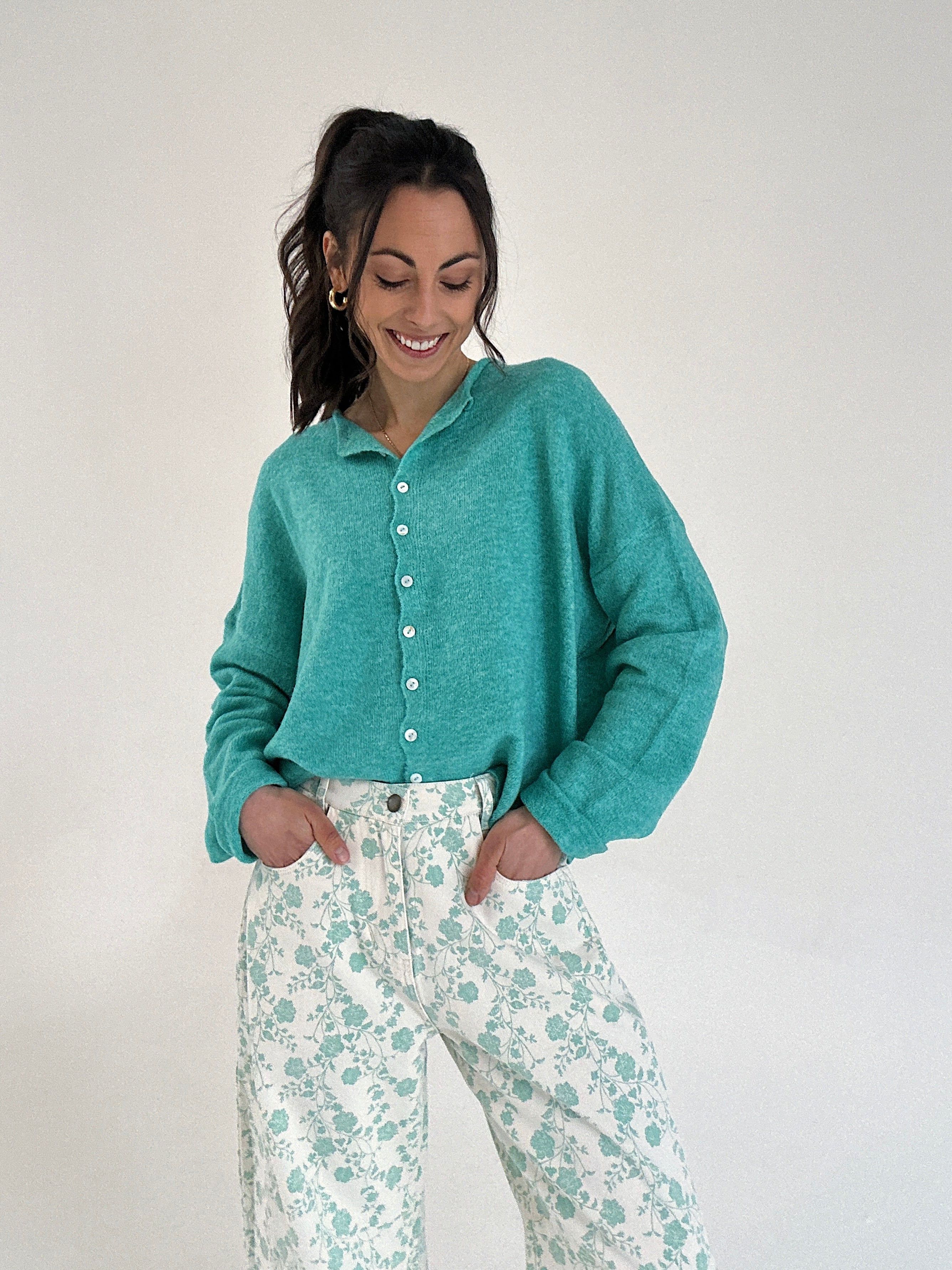 Woman wearing a teal button-up cardigan and floral pants on a white background
