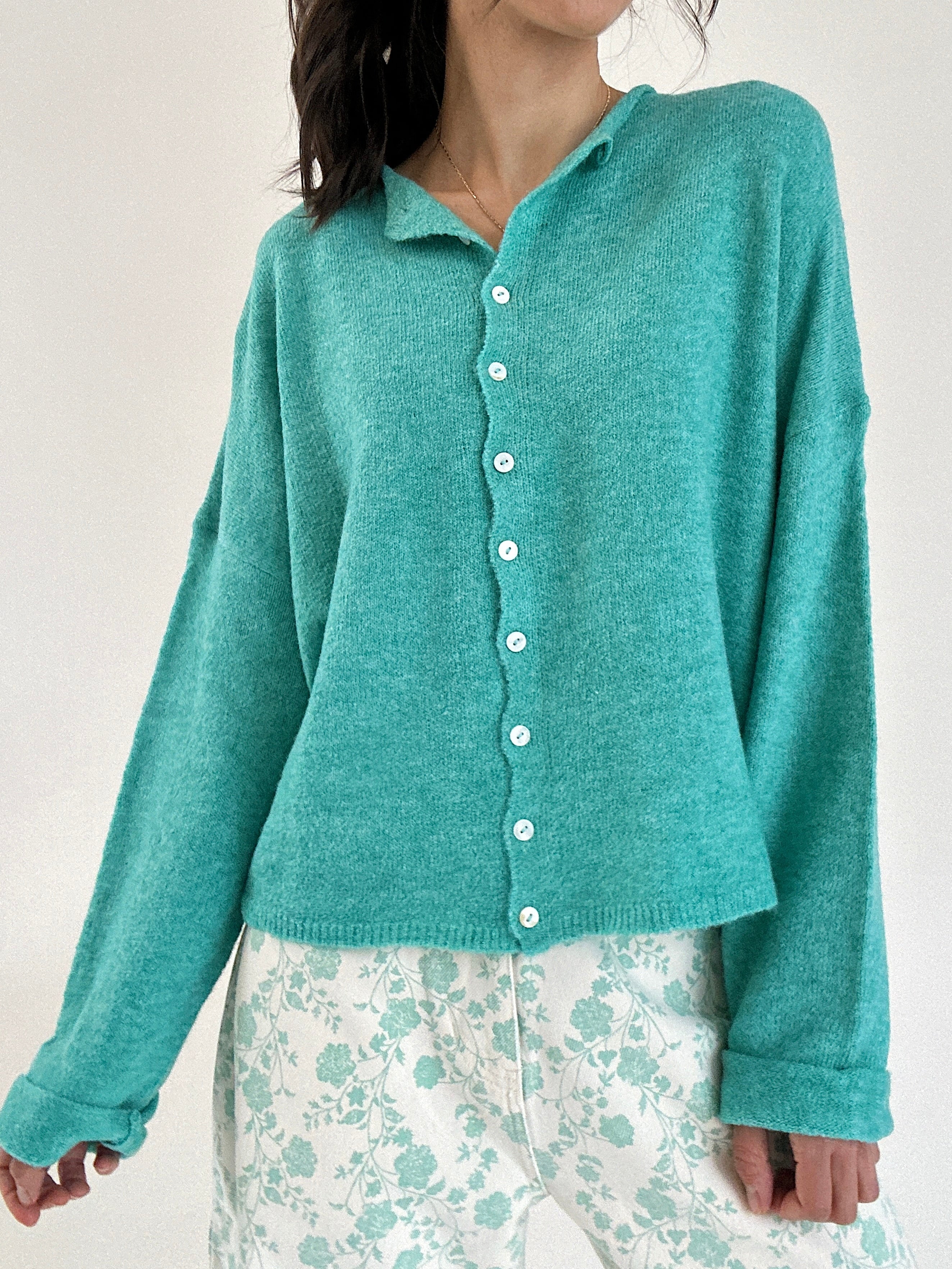Person wearing a teal cardigan over a floral outfit on a plain background