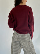 Person wearing a burgundy sweater and plaid pants against a plain background back view