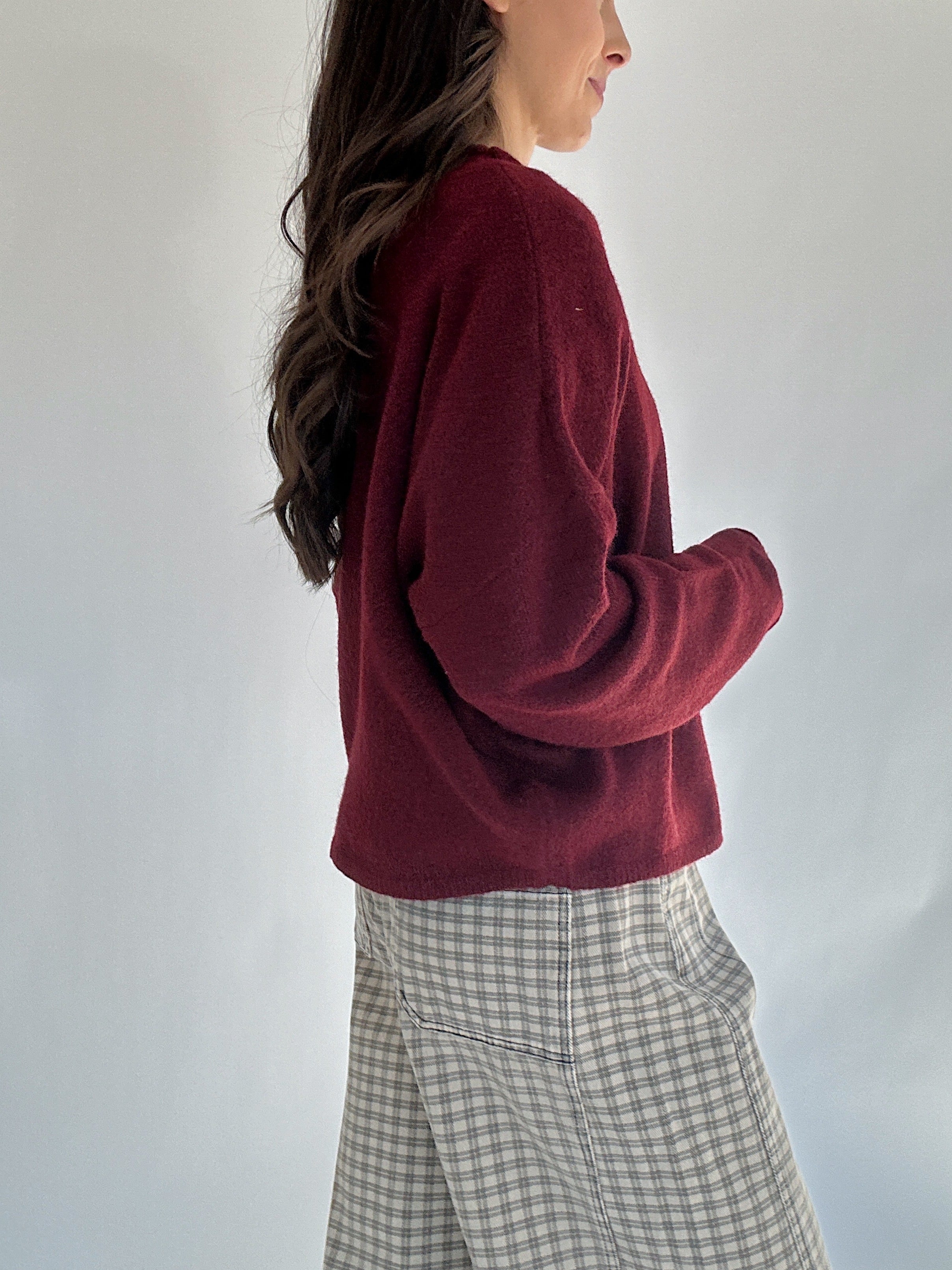 Person wearing a burgundy sweater and plaid pants against a plain background side view