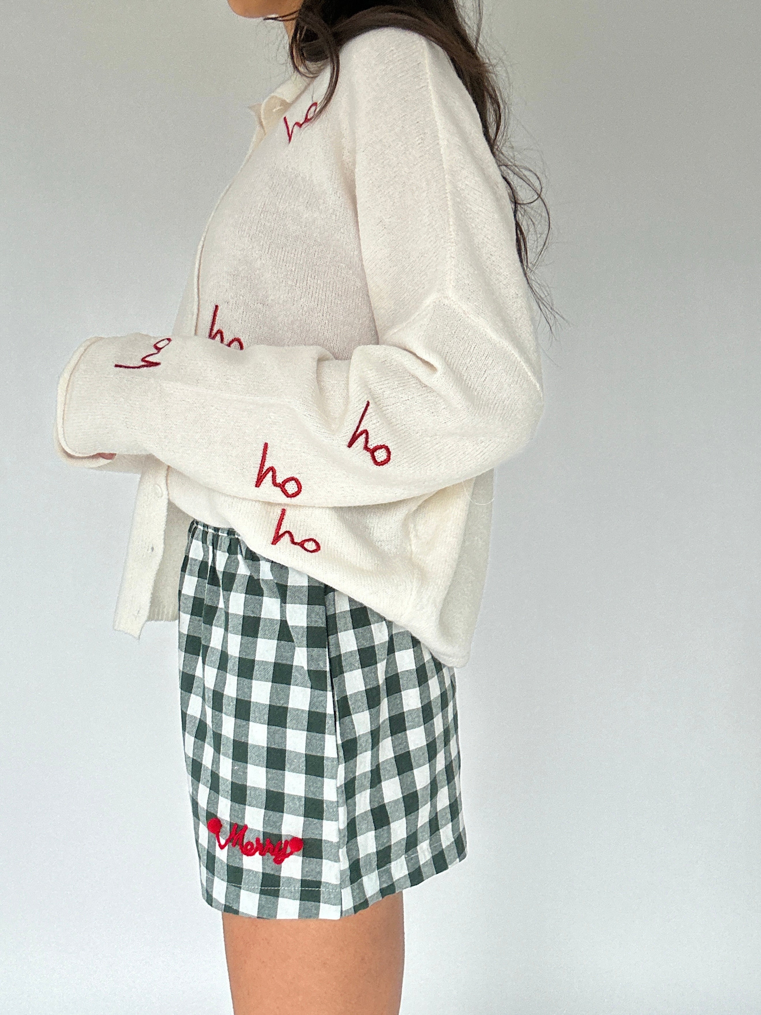 Person wearing a white sweater with red text and green checkered shorts on a plain background