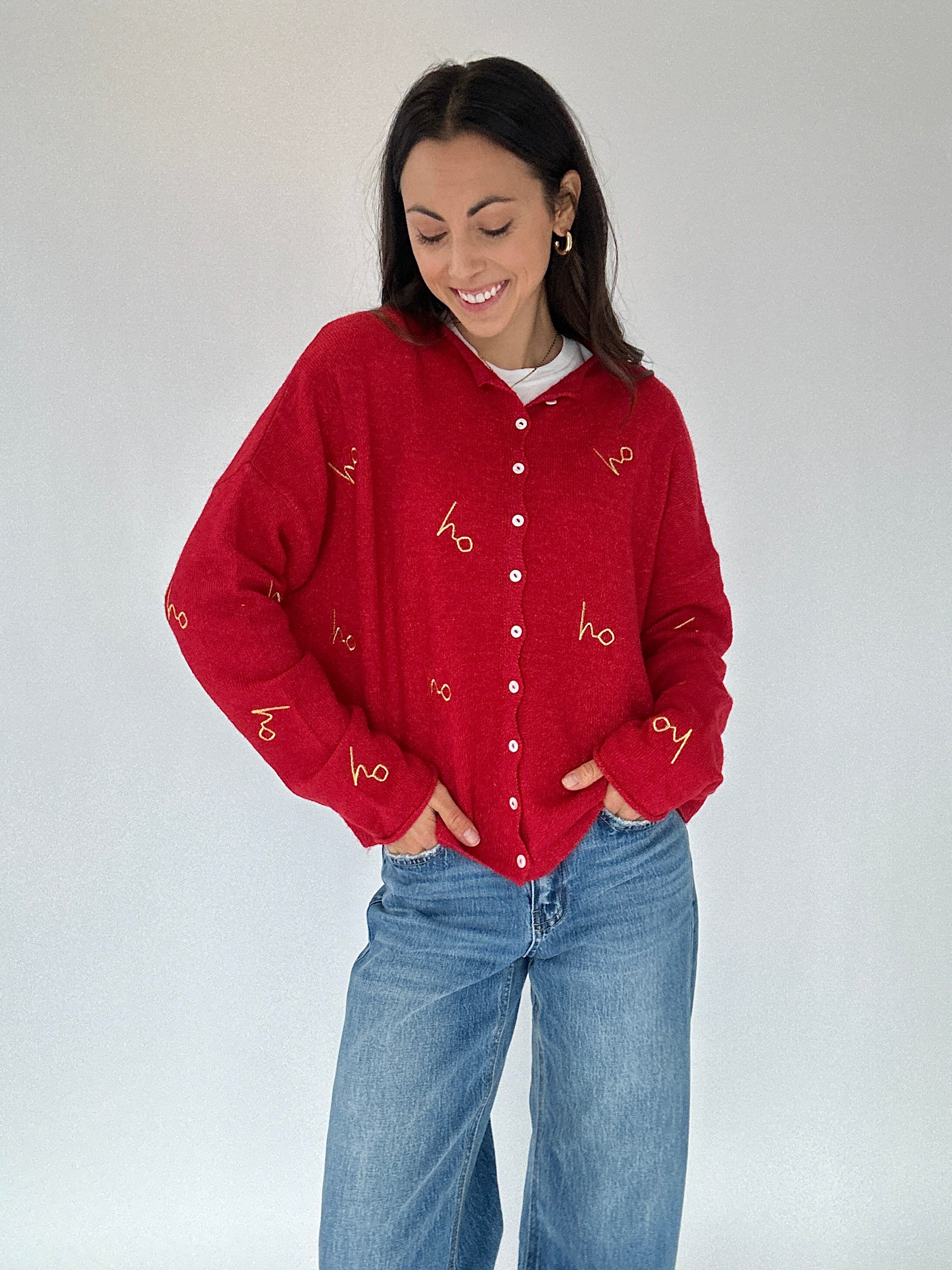 Woman wearing a red cardigan with 'ho ho ho' gold embroidered text and blue jeans on a white background