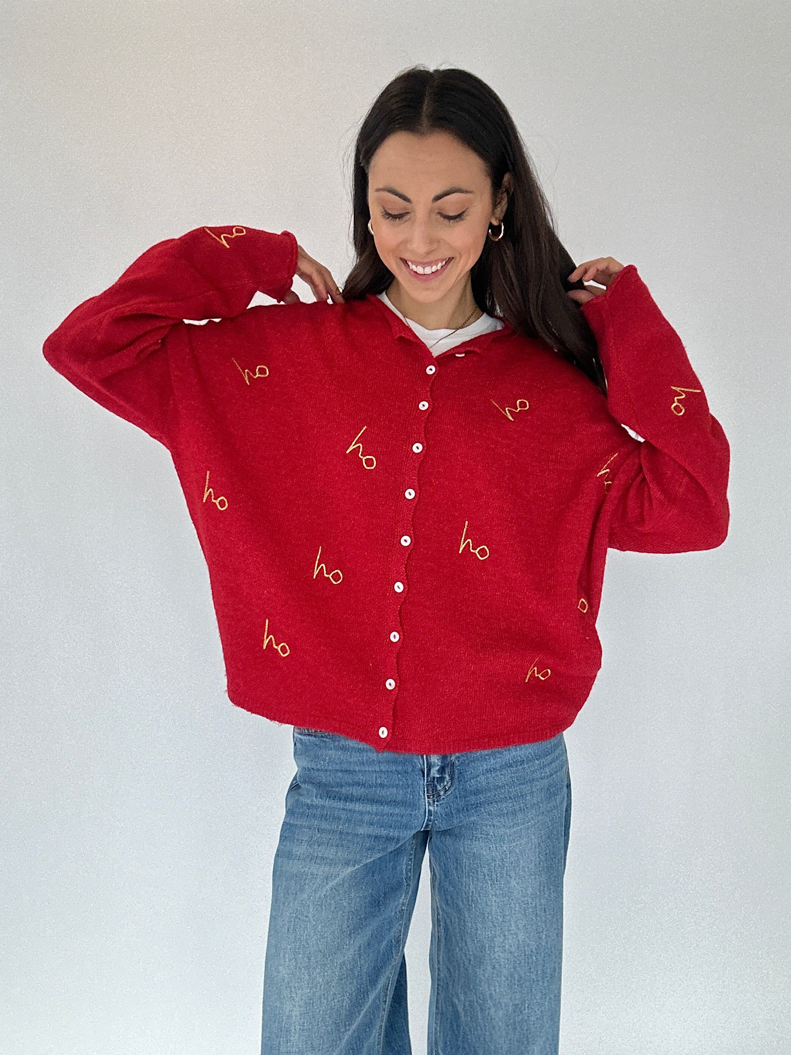 Person wearing a red cardigan sweater with gold 'ho ho ho' embroidered text on a plain background