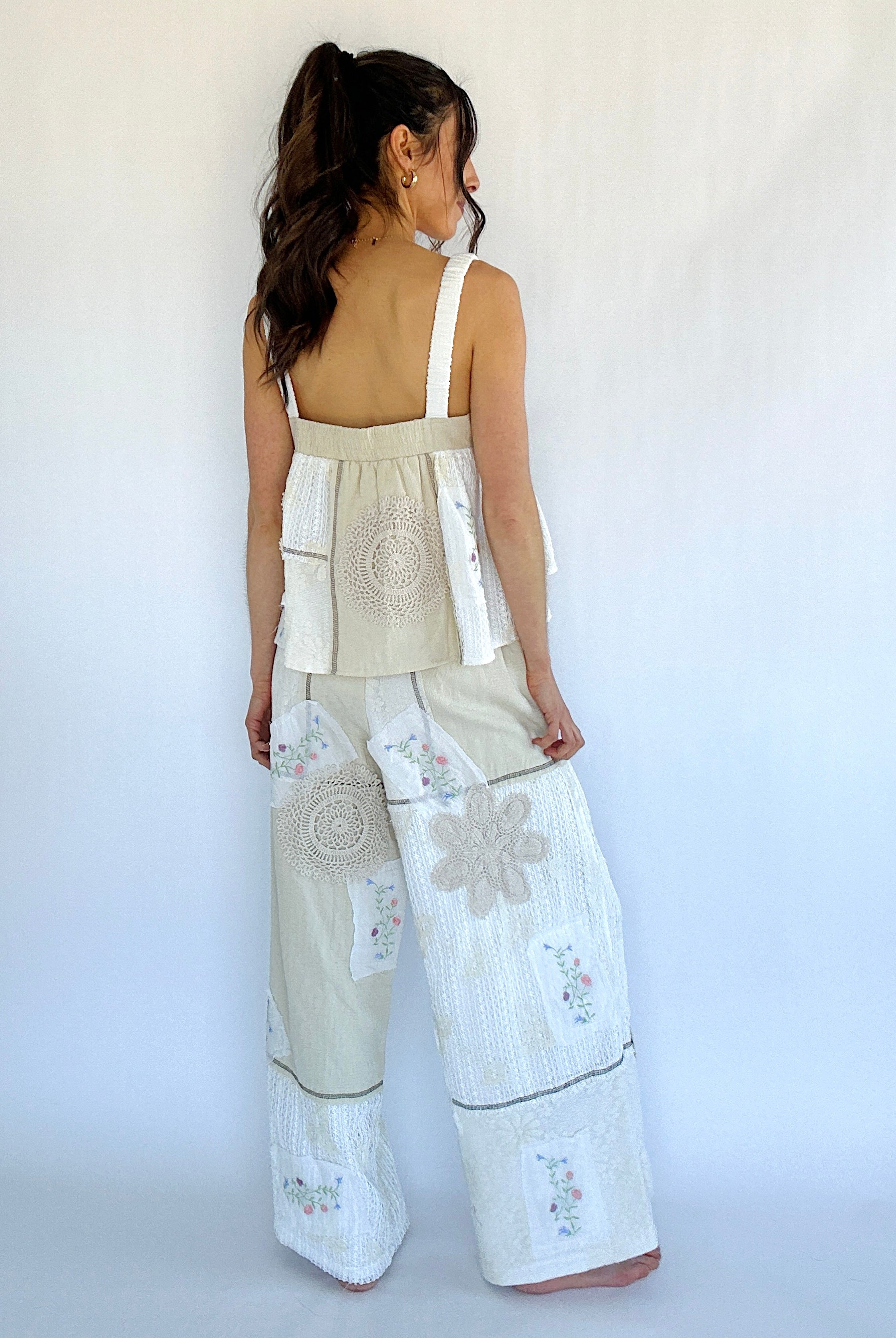 Woman wearing a beige sleeveless top and white pants with floral patterns against a white background
