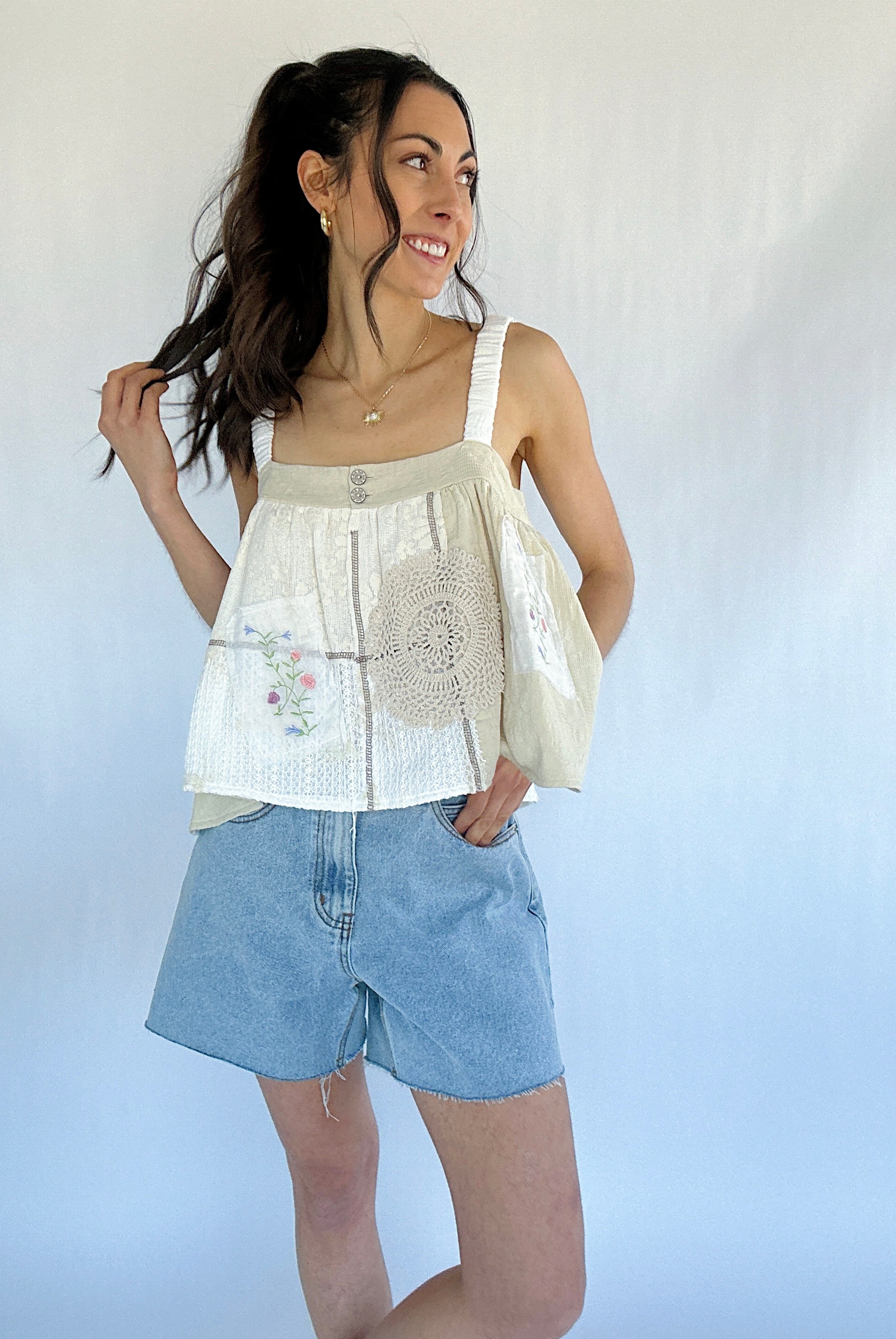 Woman wearing a sleeveless top with a floral pattern and denim shorts against a plain background